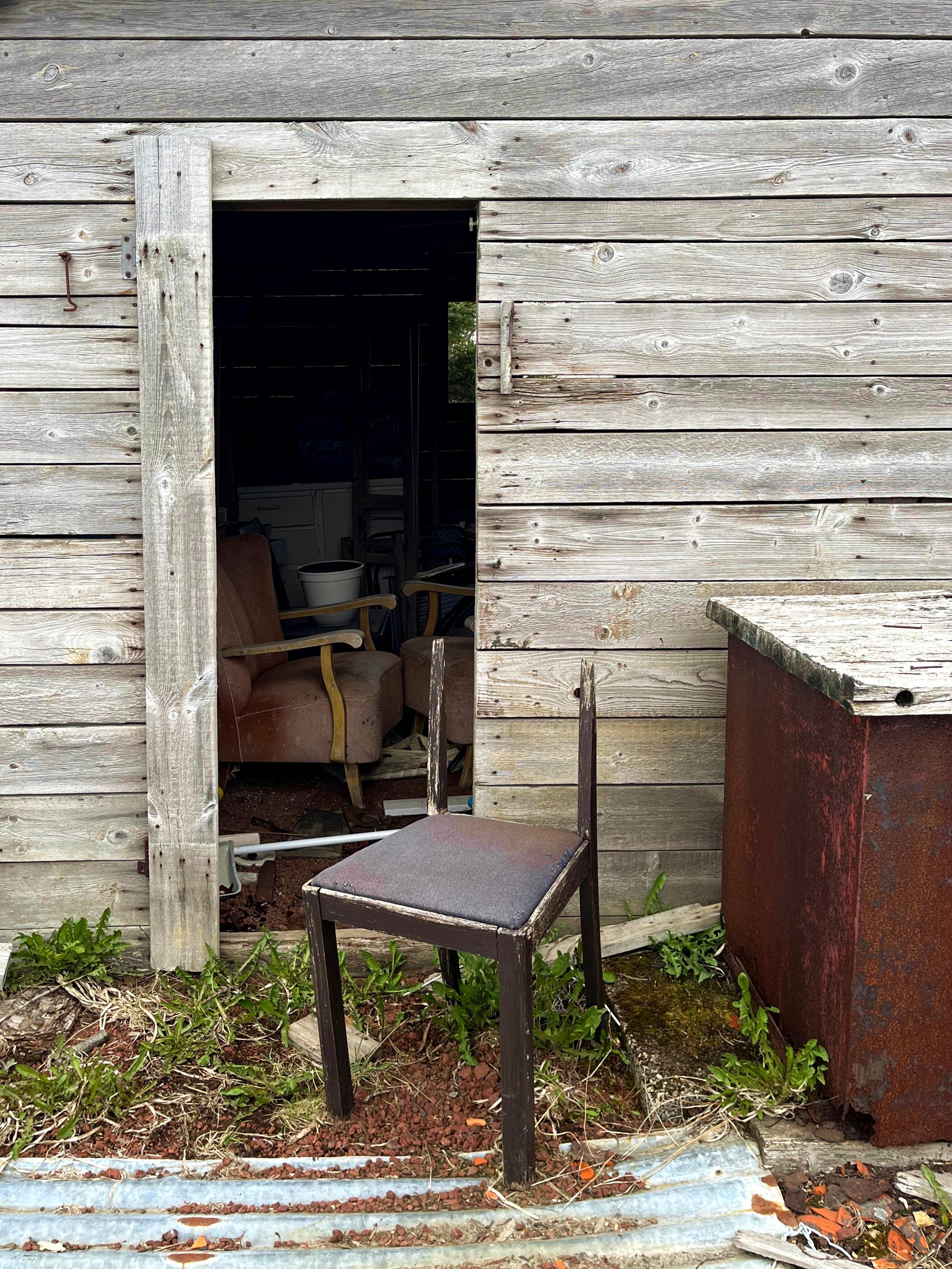 A broken old chair in front of an abandoned storage shed.
