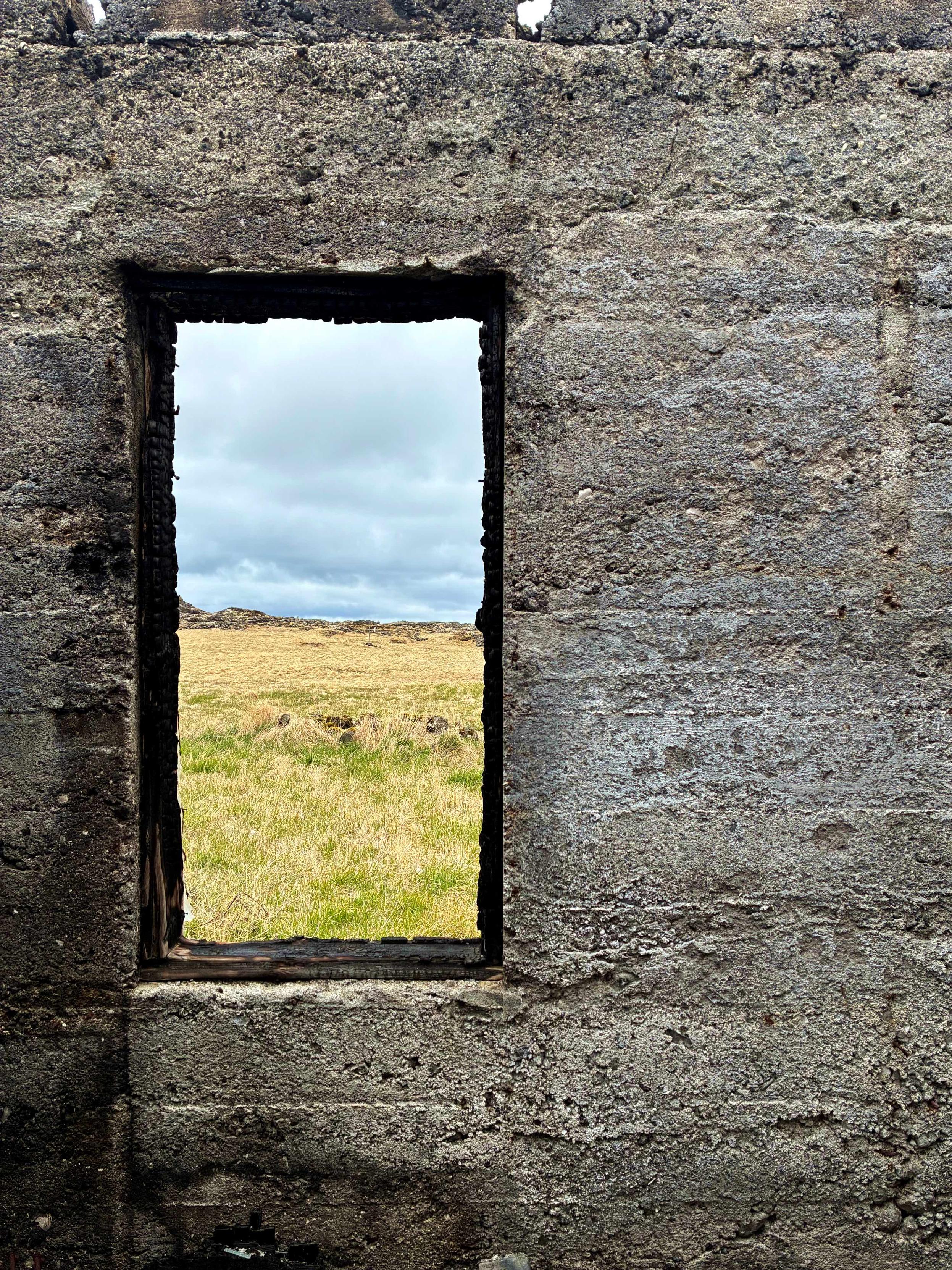 A window in an abandoned building looking out at a field.