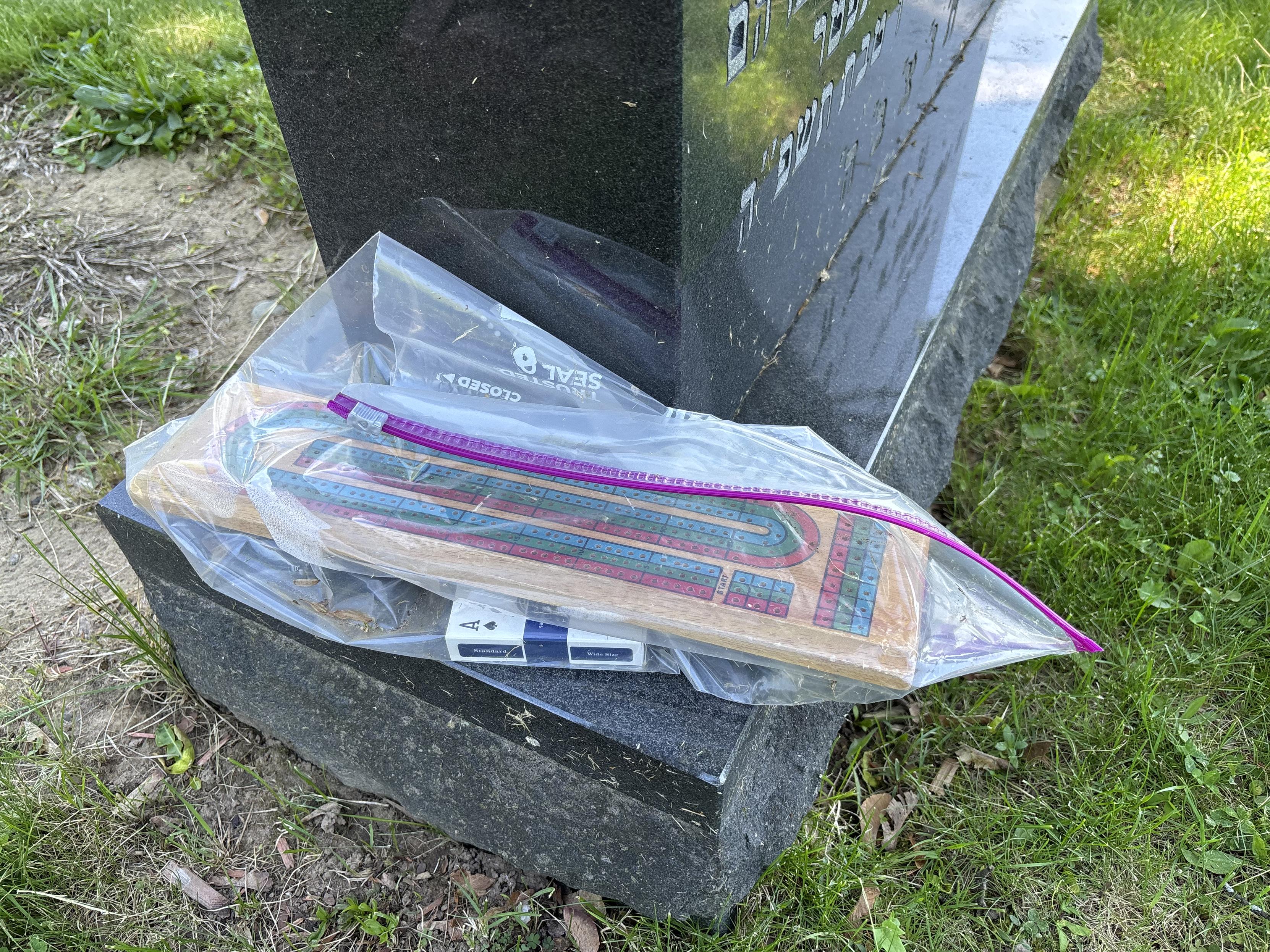 cribbage board and deck of cards in a plastic bag on a gravestone