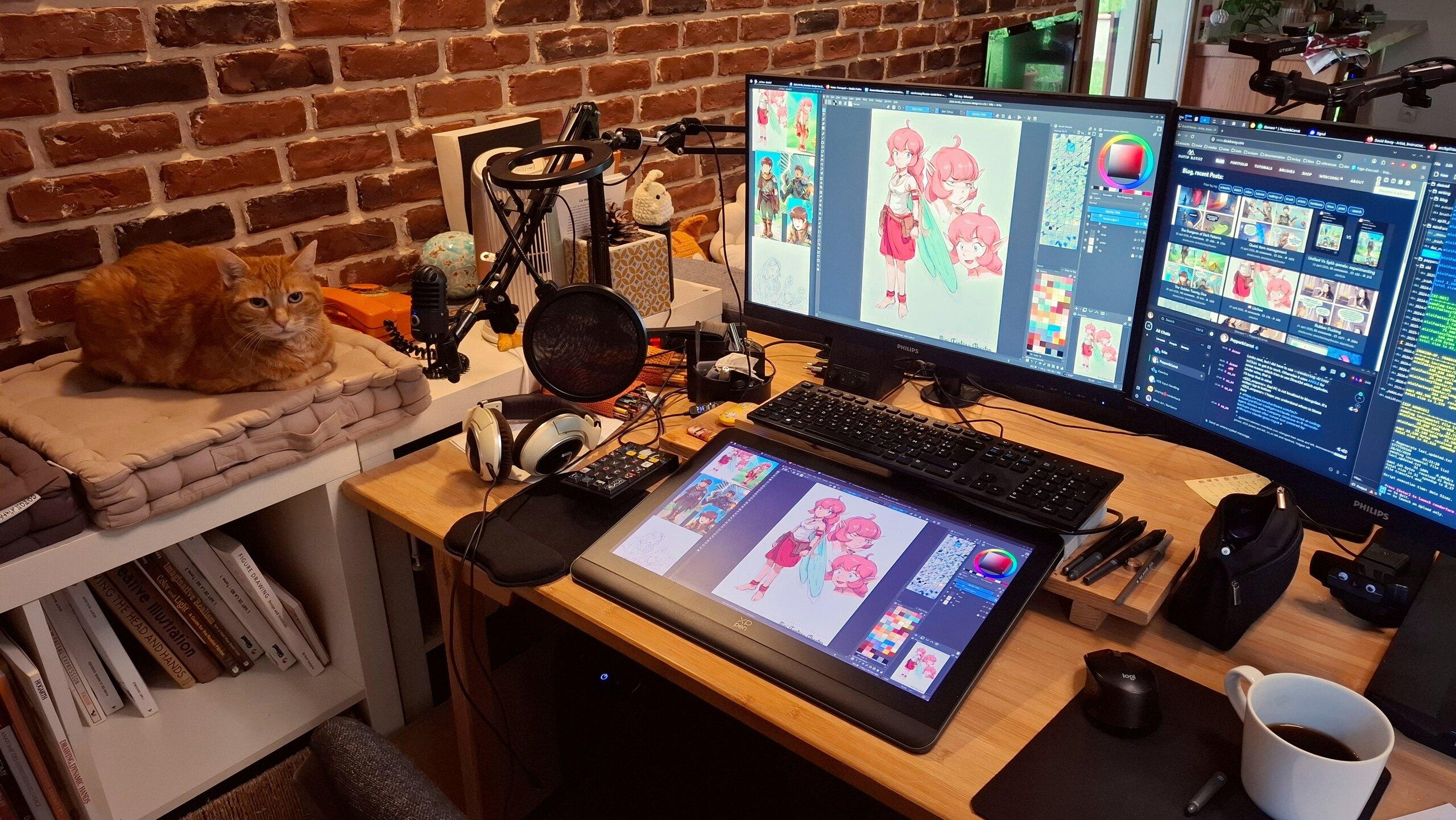 A photo of my workstation, three display: one of them is a drawing tablet with a display. On the screen: while coloring in Krita the character Litchee the Pink Fairy of my weekly comic series Mini Fantasy Theater. My cat, a red tabby, look at the camera while comfortably sited on his pillow, disposed strategically on the side of my desk for him to not sleep on my keyboard.