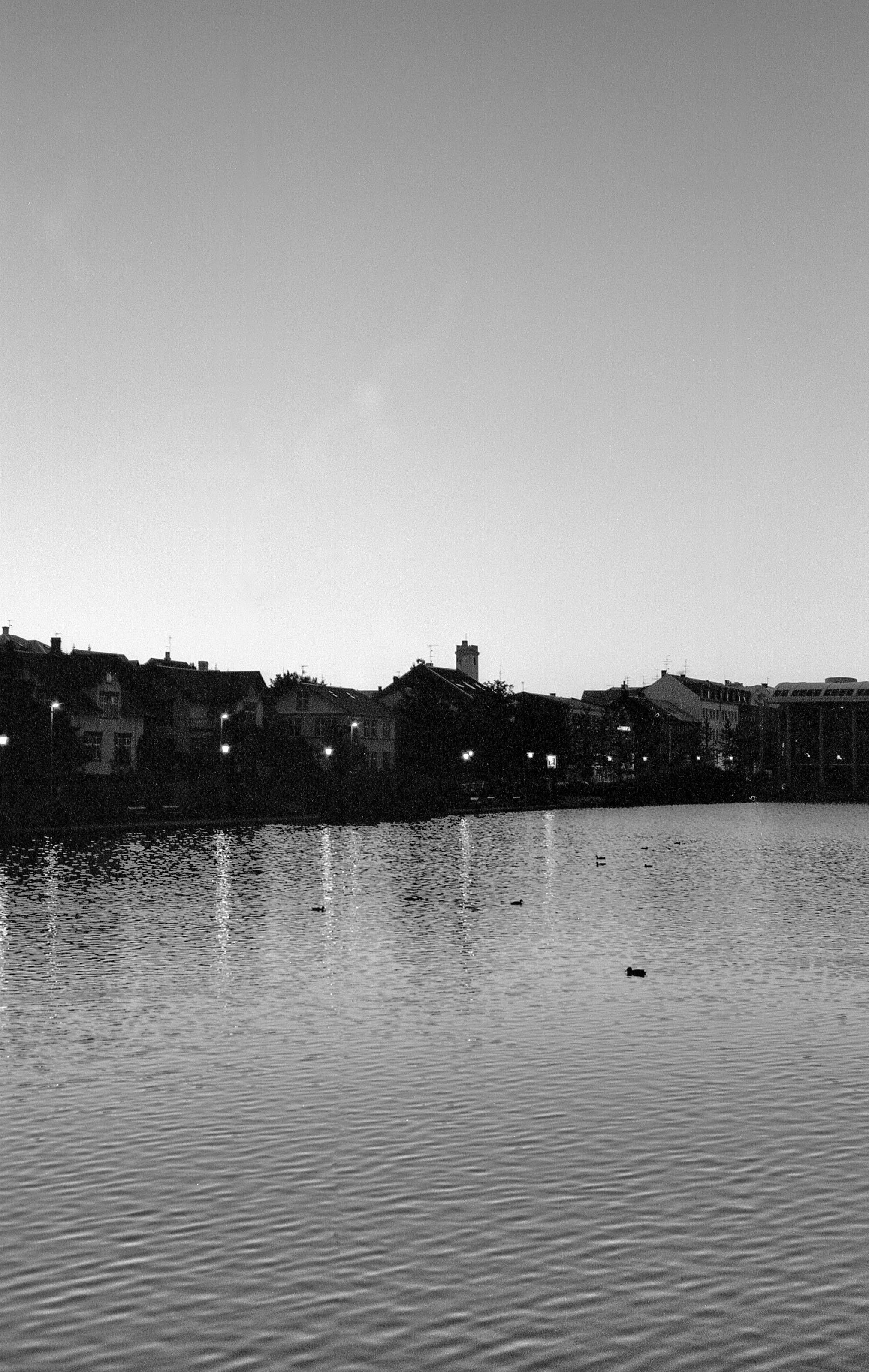 A photo of the pond in the Reykjavík city centre. The buildings are in silhouette as the sun sets.