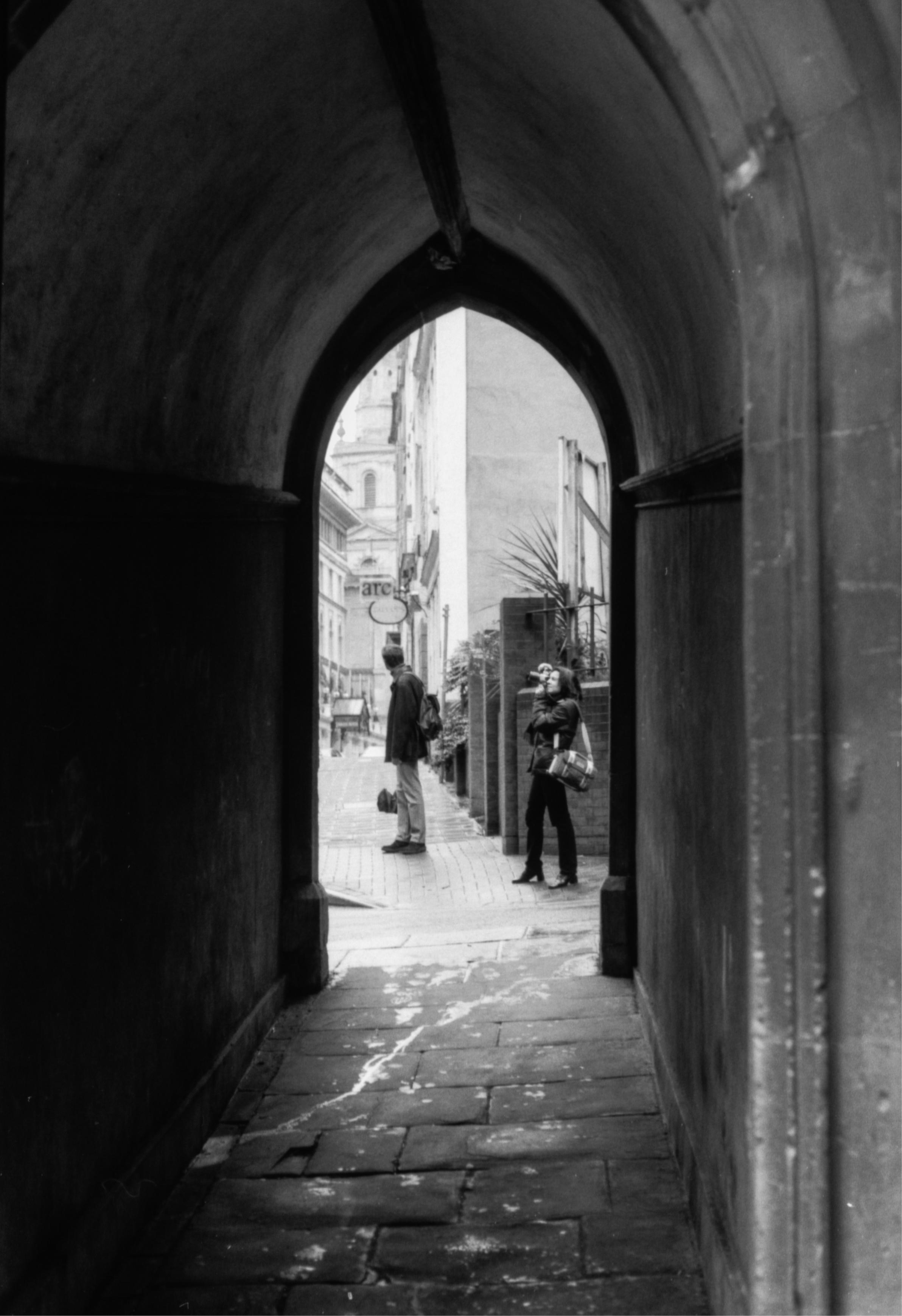 A black and white photo taken through an arch in Bristol city centre. A woman is on the other side taking photos of the architecture.