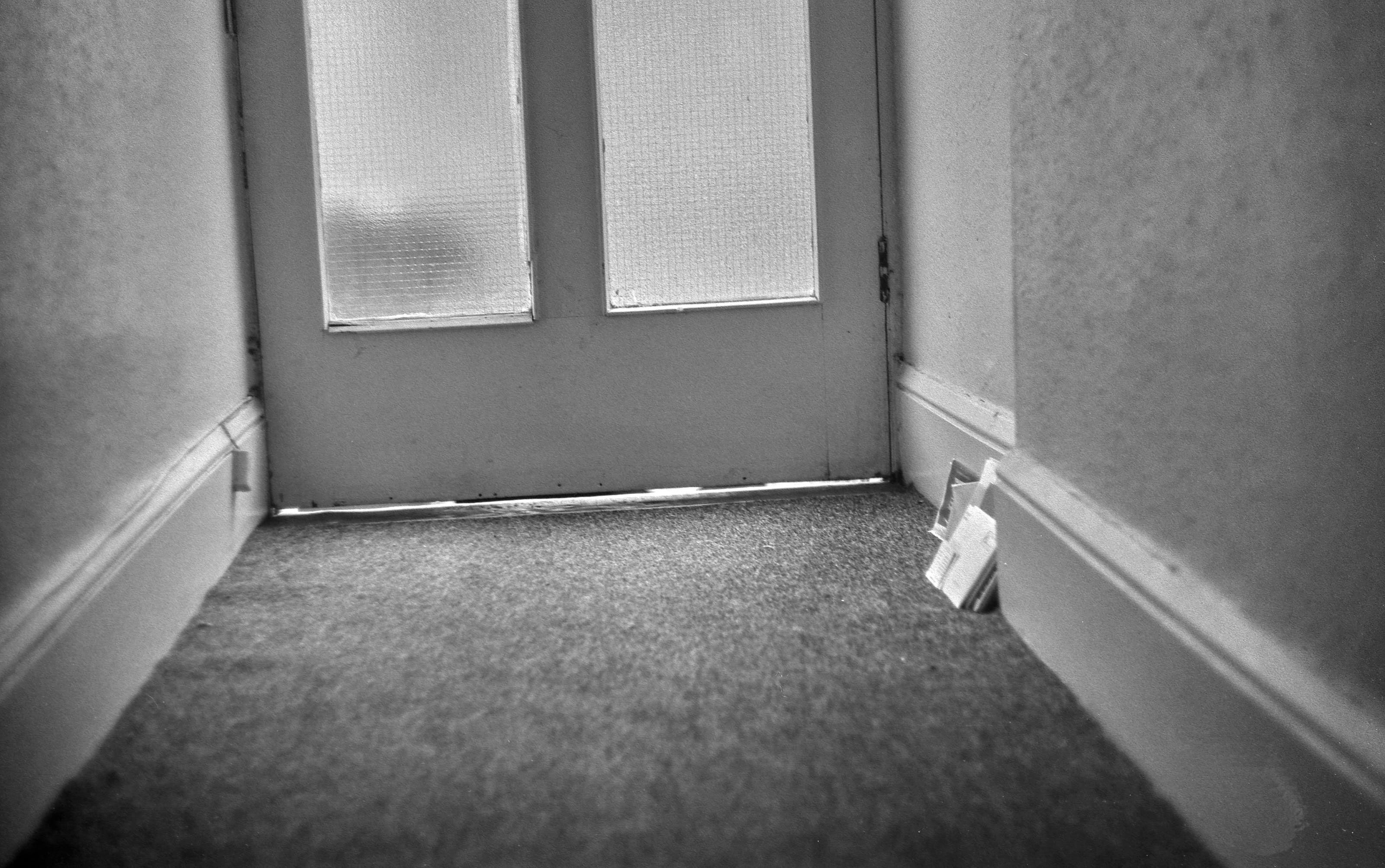 Mail is stacked up against the wall by a very shoddy front door.