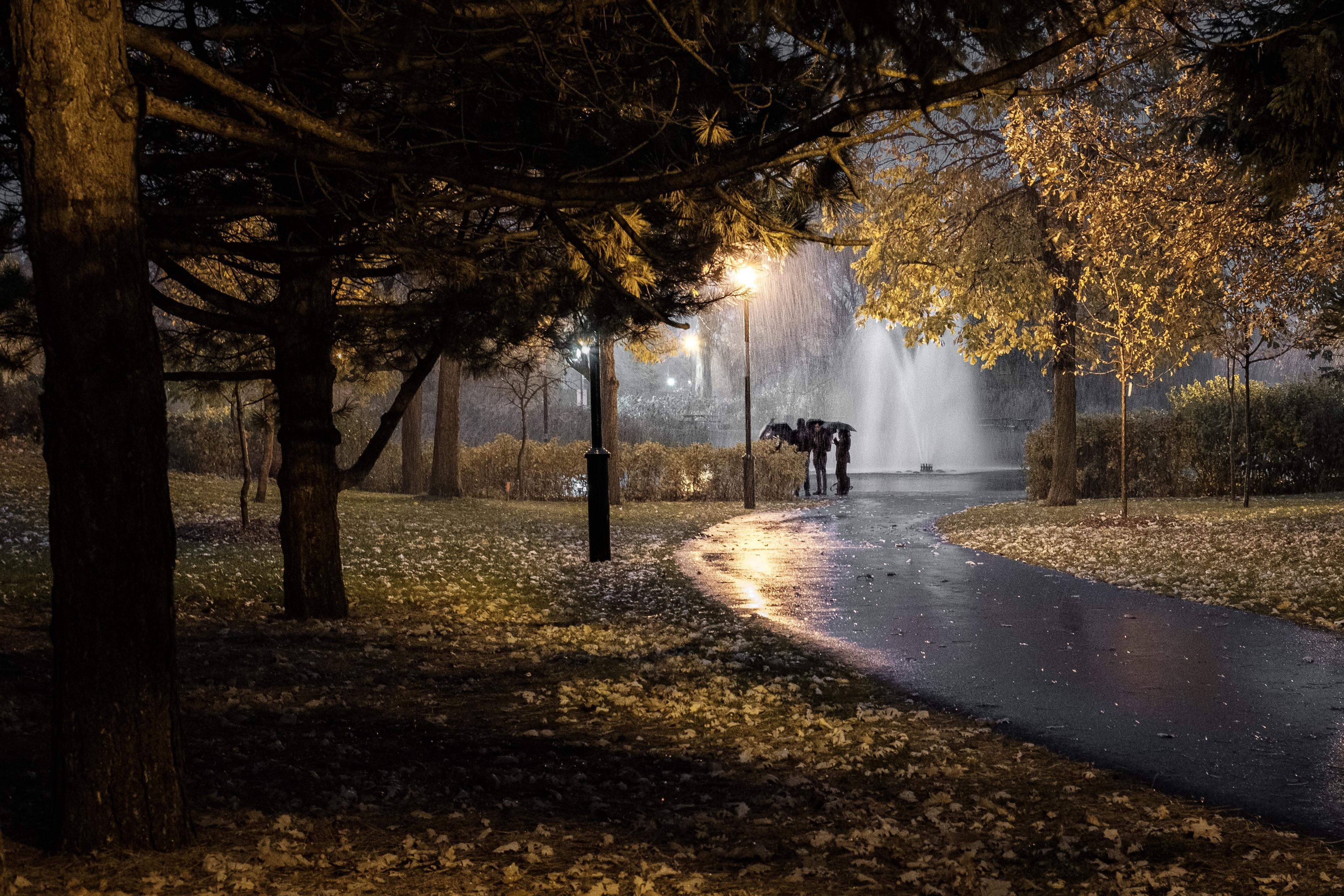 People meet in the rain, under the cover of their umbrellas, in Parc Jarry, Montréal.