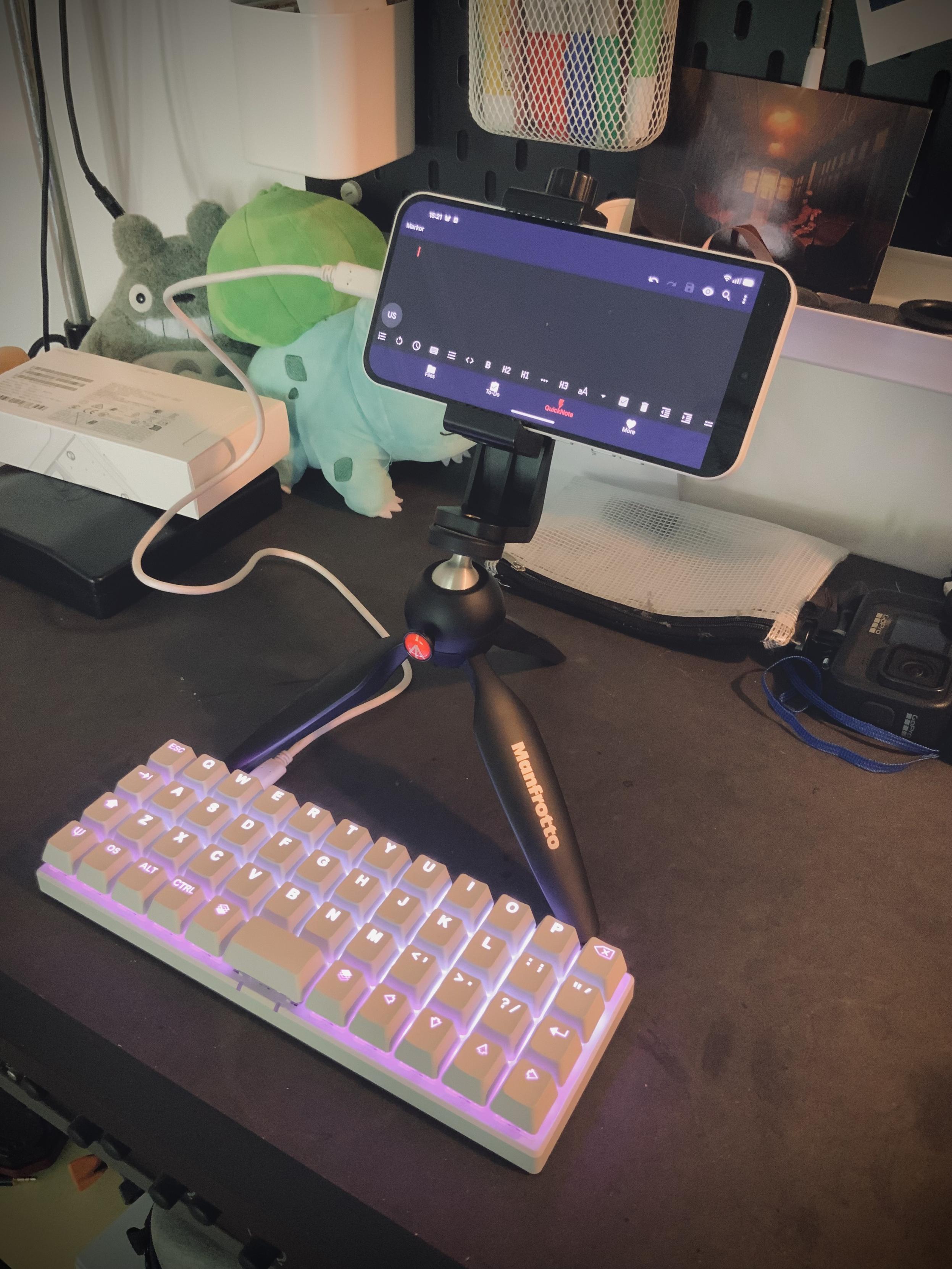 A phone in a clamp on a tiny tripod, connected to a small mechanical keyboard with no number row
