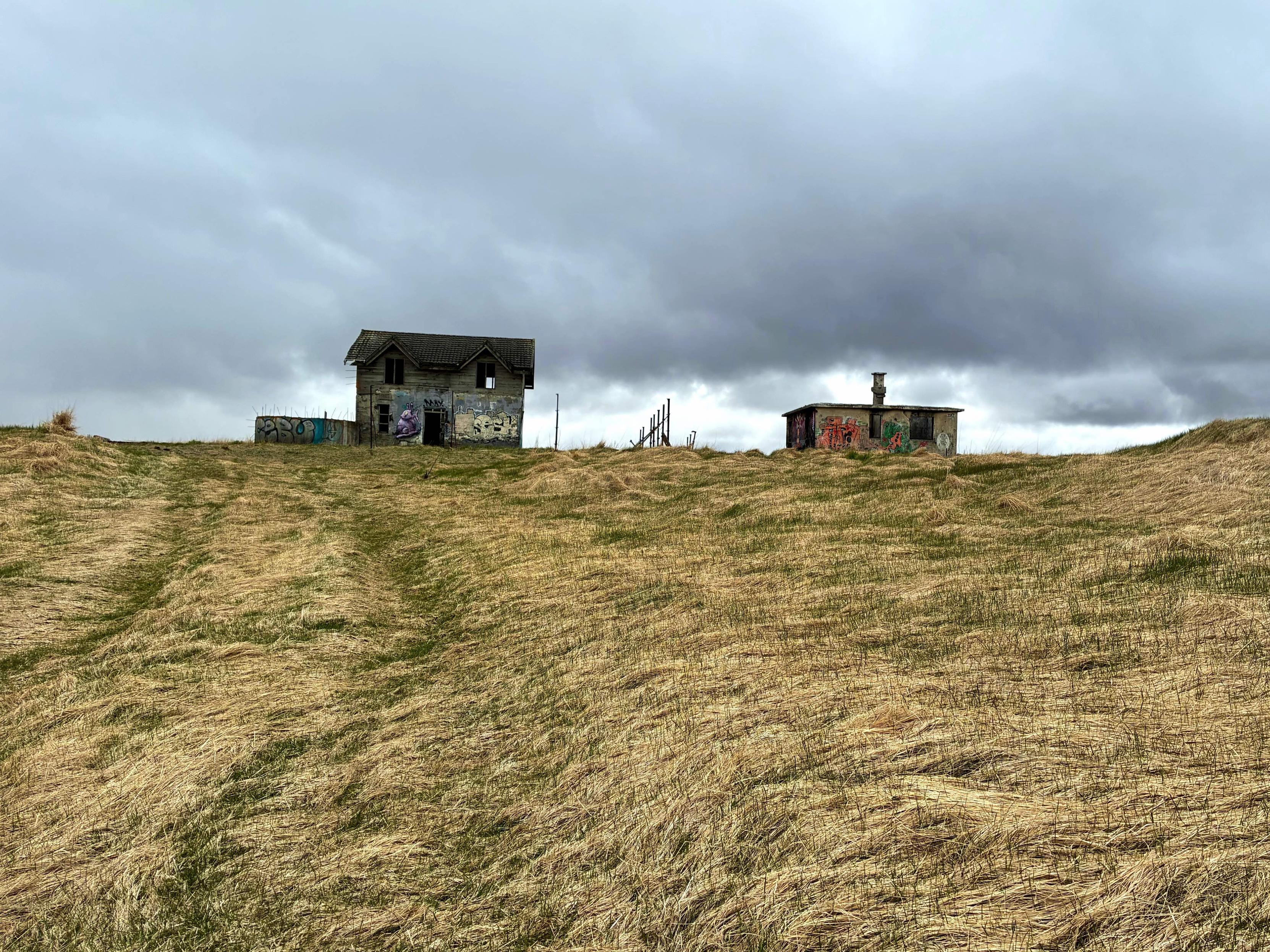 Two abandoned concrete houses in a field.