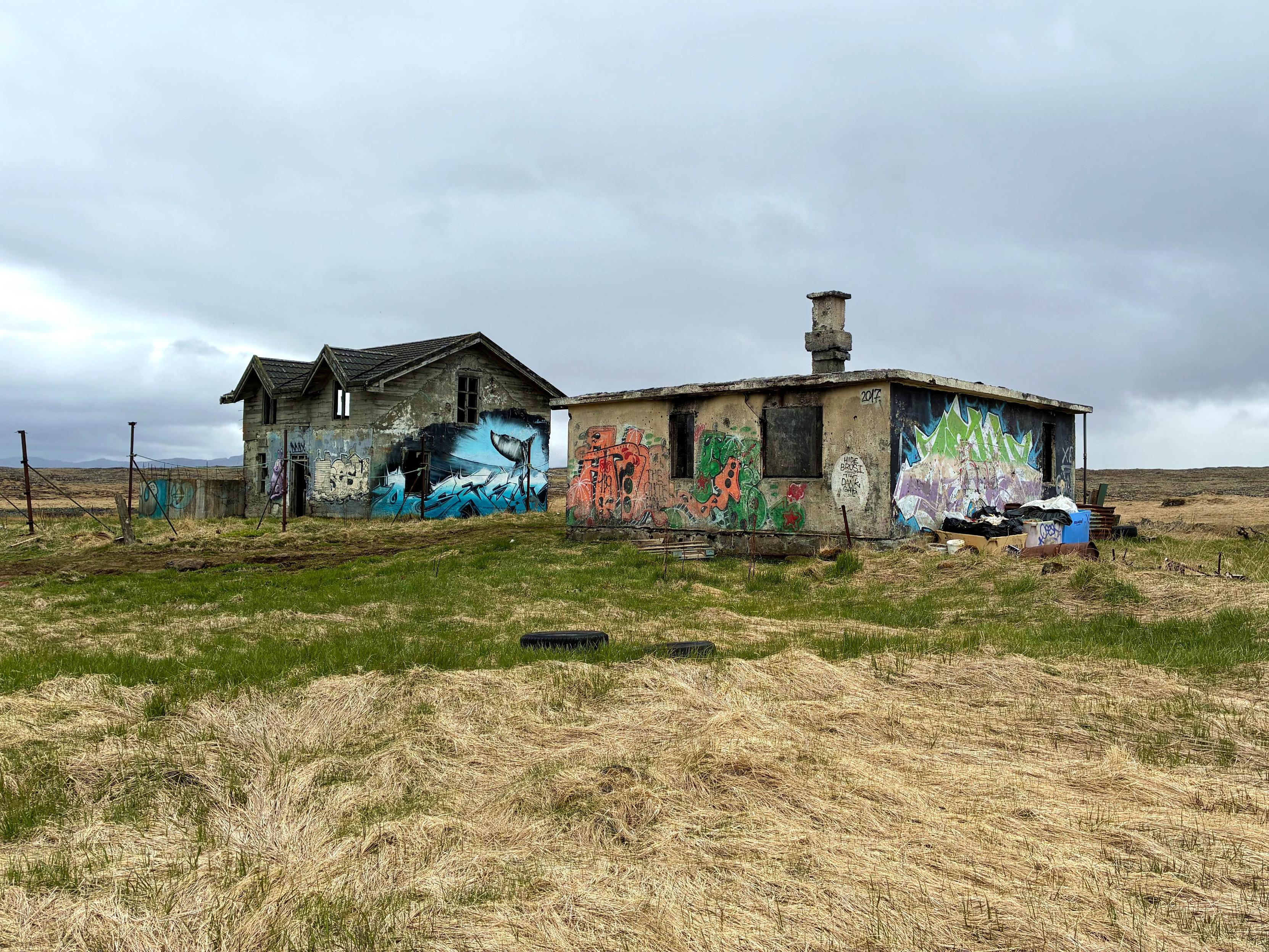 Abandoned farm surrounded by grass with mountains at a distance.