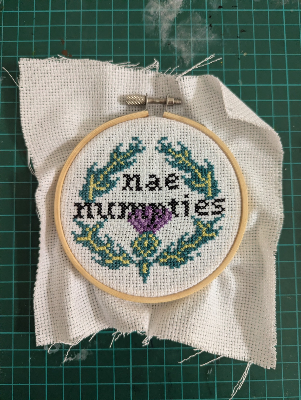 An embroidery of a thistle with "nae numpties" written inside