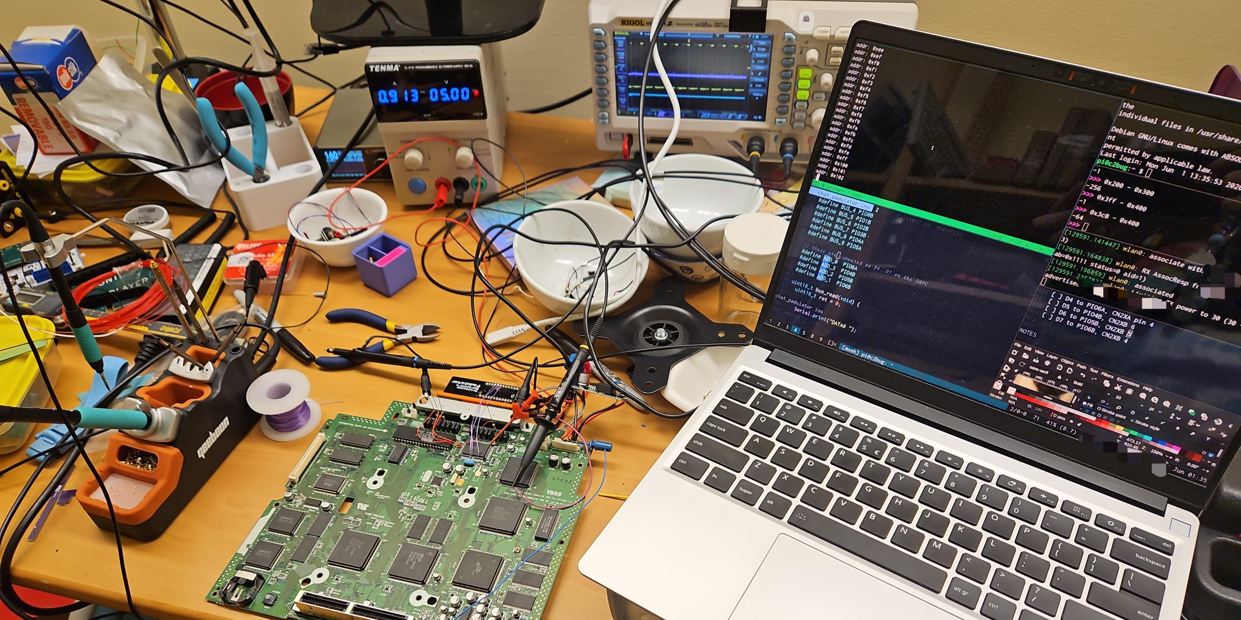 A wider shot of the messy workbench. We now see laptop, soldering gear, bench power supply, oscilloscope, assorted hand tools... this is one messy desk user.