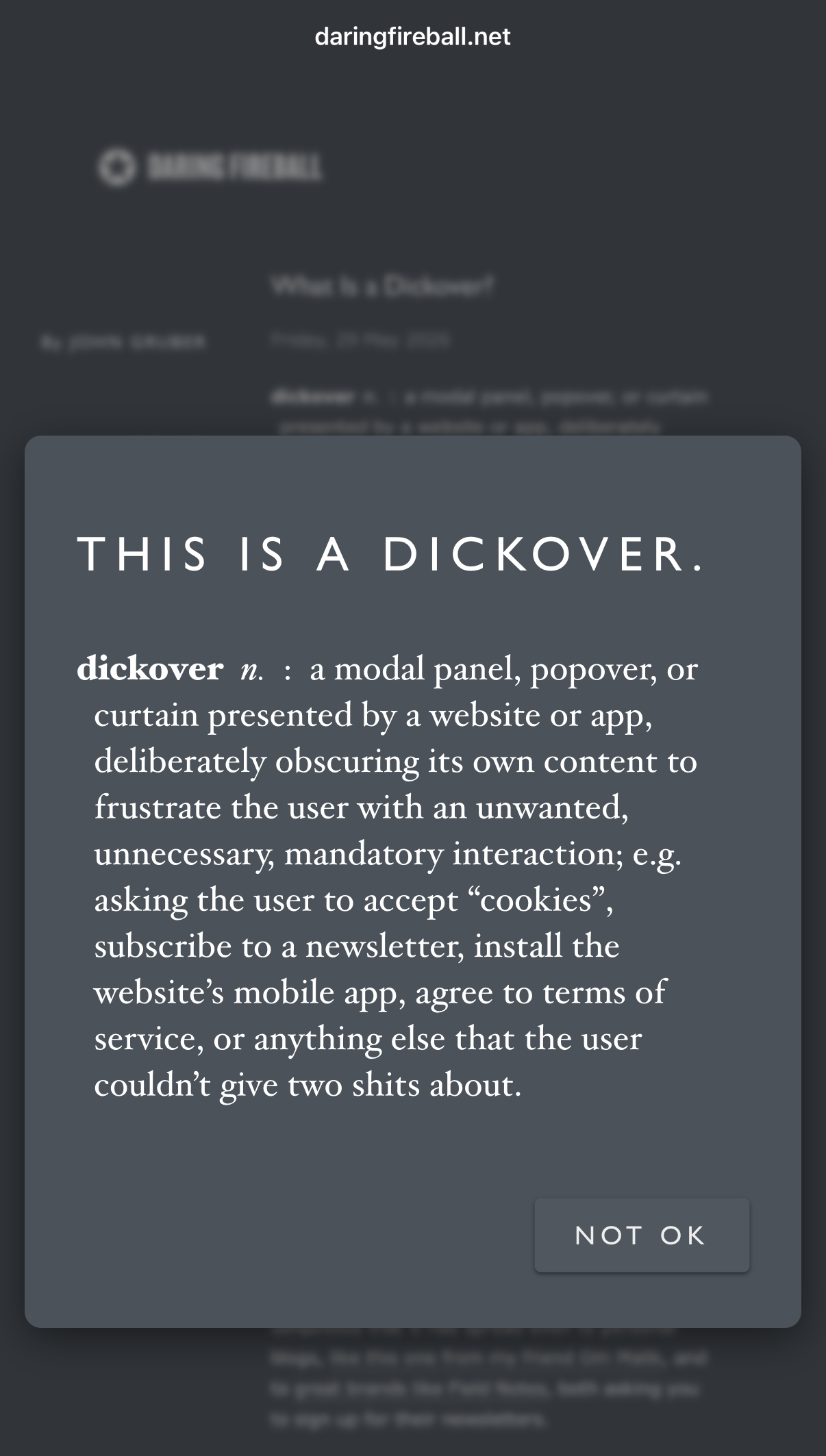 A screenshot of the website daringfireball.net featuring a large, dark grey pop-up window in the foreground. The pop-up contains the text "THIS IS A DICKOVER." followed by the definition: "dickover n. : a modal panel, popover, or curtain presented by a website or app, deliberately obscuring its own content to frustrate the user with an unwanted, unnecessary, mandatory interaction; e.g. asking the user to accept 'cookies', subscribe to a newsletter, install the website's mobile app, agree to terms of service, or anything else that the user couldn't give two shits about." A button in the bottom right corner of the pop-up reads "NOT OK". The blurred background shows the website header "DARING FIREBALL" and an article titled "What is a Dickover?".