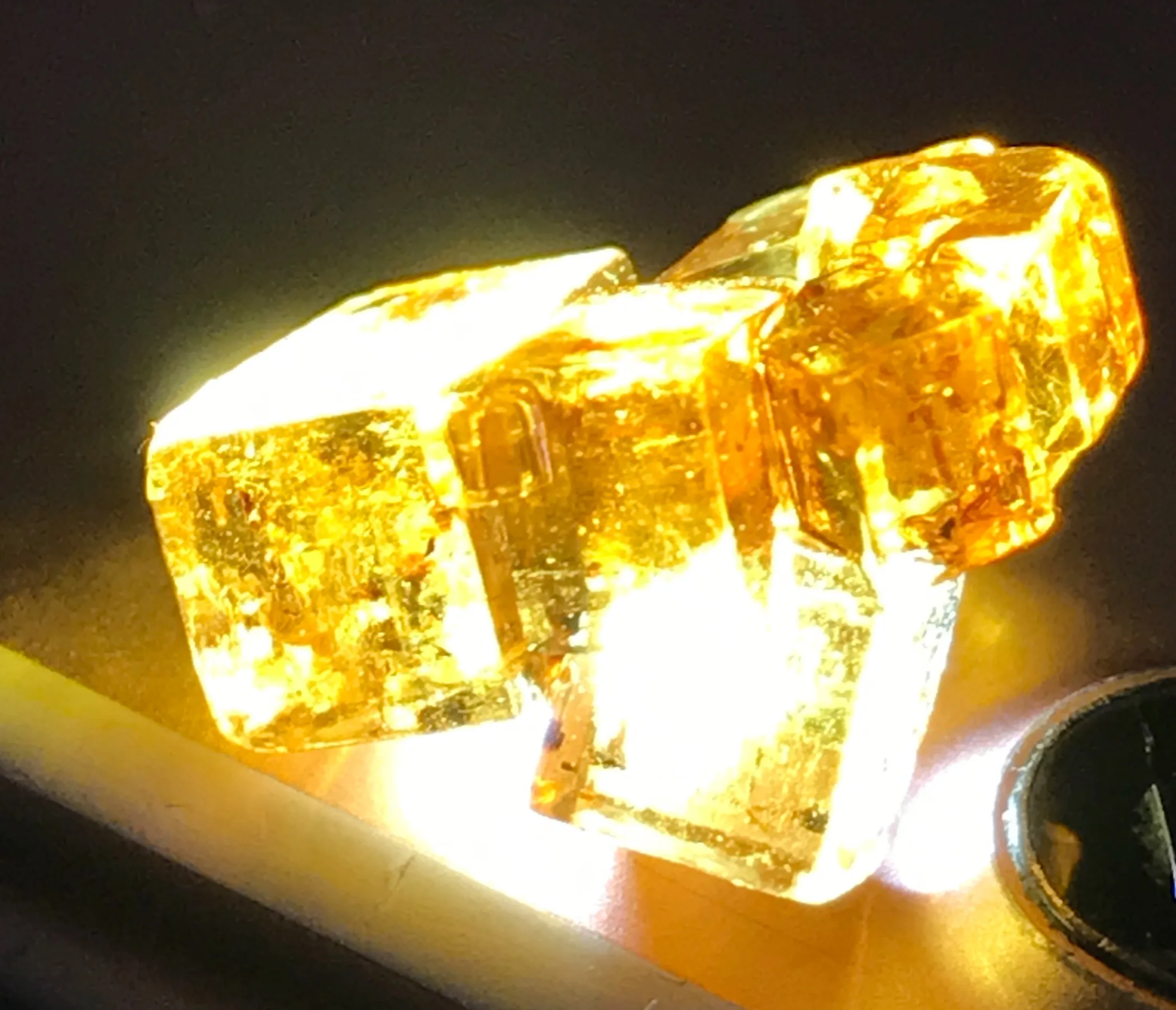 A photo of a batch of soy sauce generated salt crystals sitting on top of an iphone torchlight, looking like crystal gold lit from within.