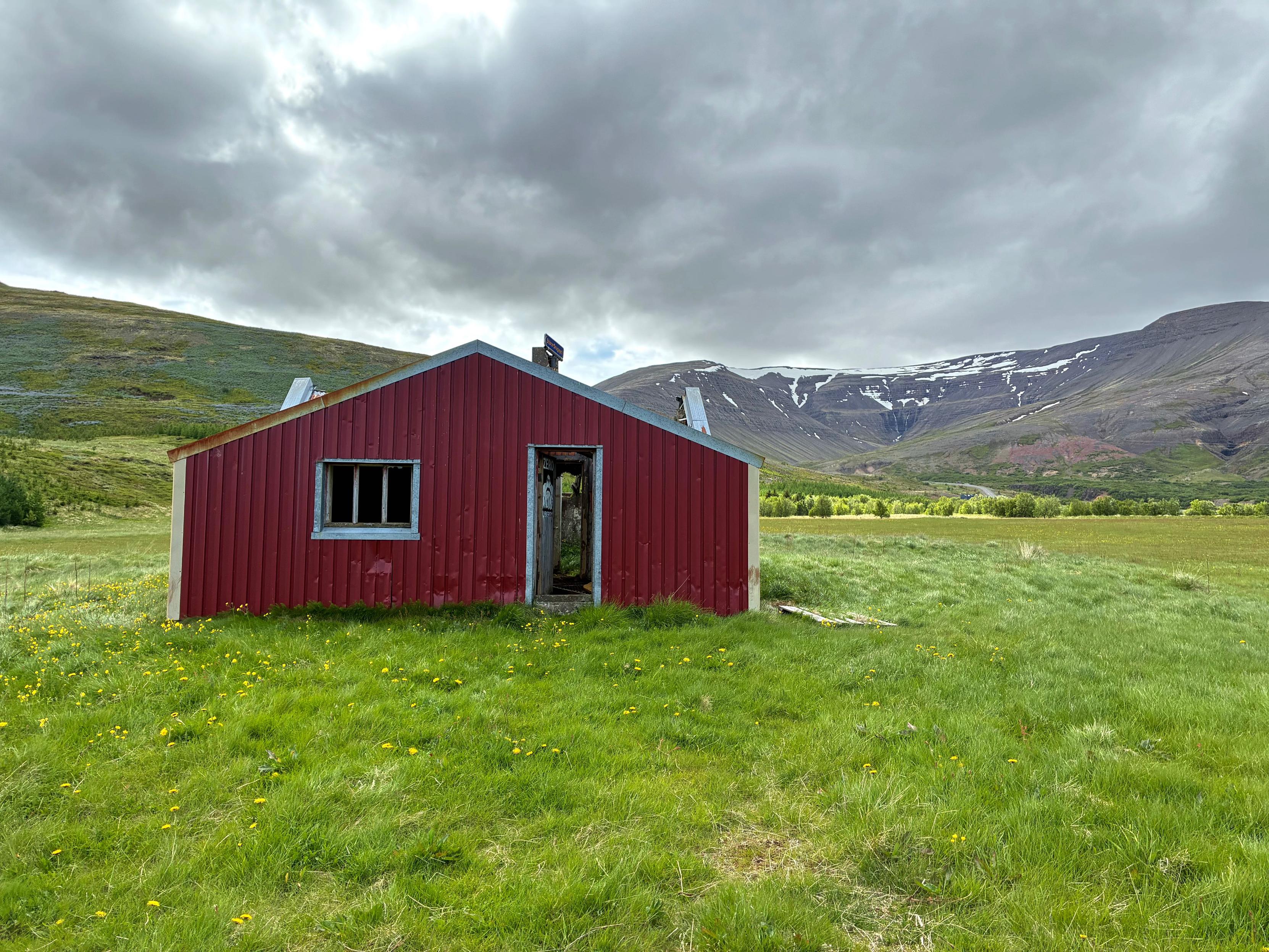 An abandoned red house with a mountain in the background.
