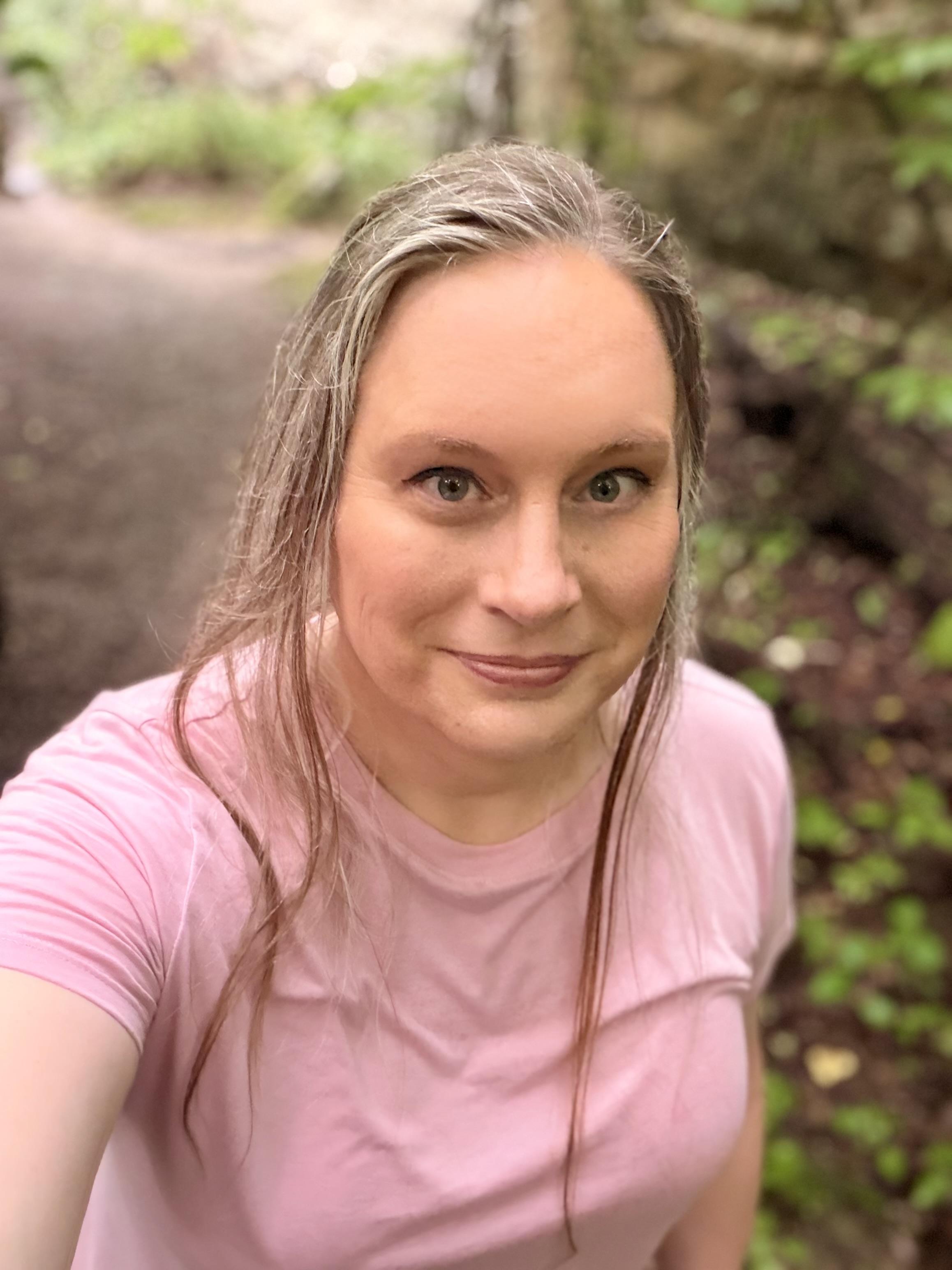 Selfie of a sweaty woman with her long hair pulled back into a pony tail and a few strands loose up front. She has grown increasingly frustrated with having to repeated climb the same hill to get a cellular phone signal. (Slightly edited using Apple cleanup tool to remove a wrinkly forehead from manually lifting eyebrows in the selfie pose.)