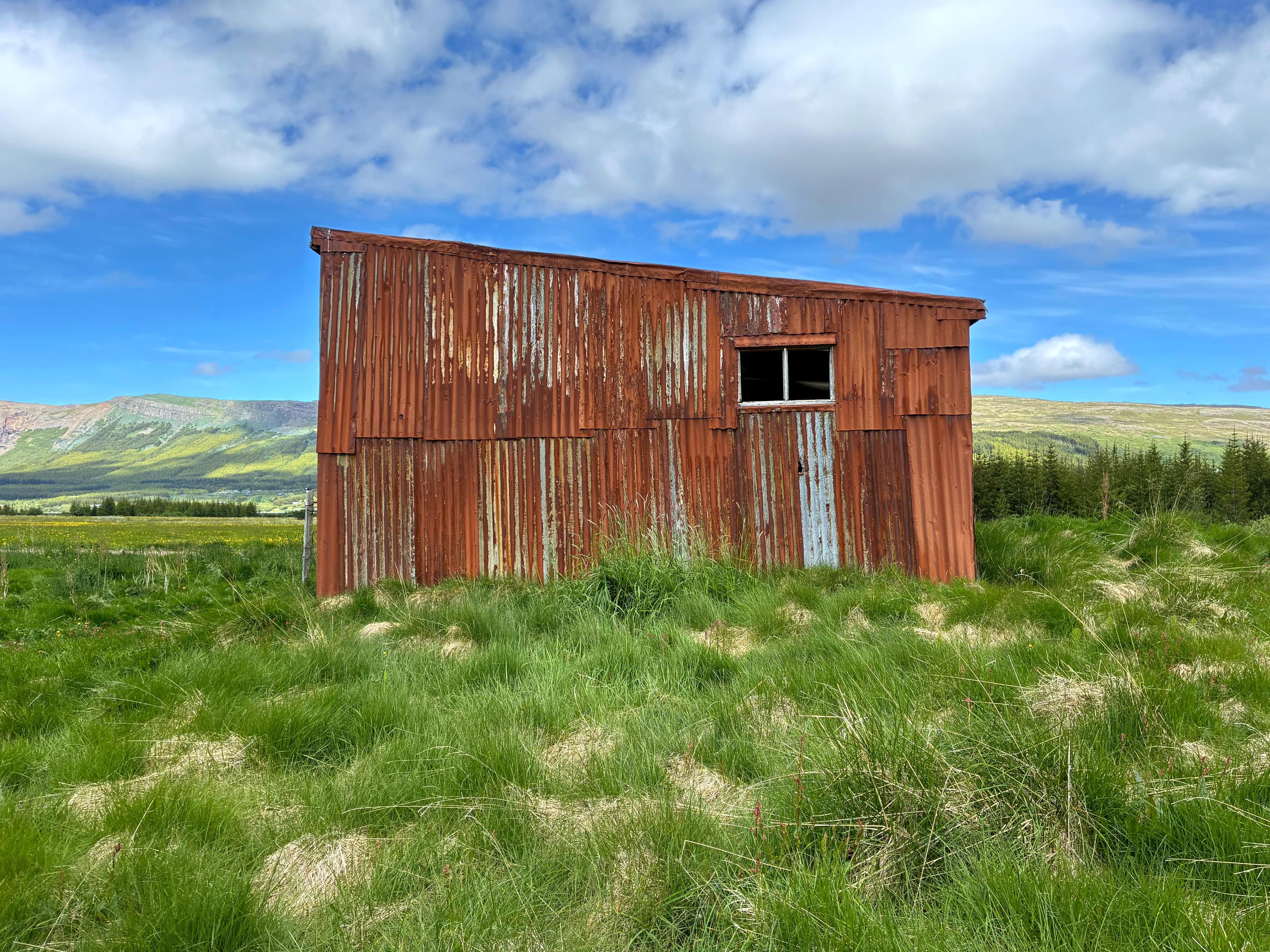 A very rusty shed with a small window and a beautiful mountain in the background.