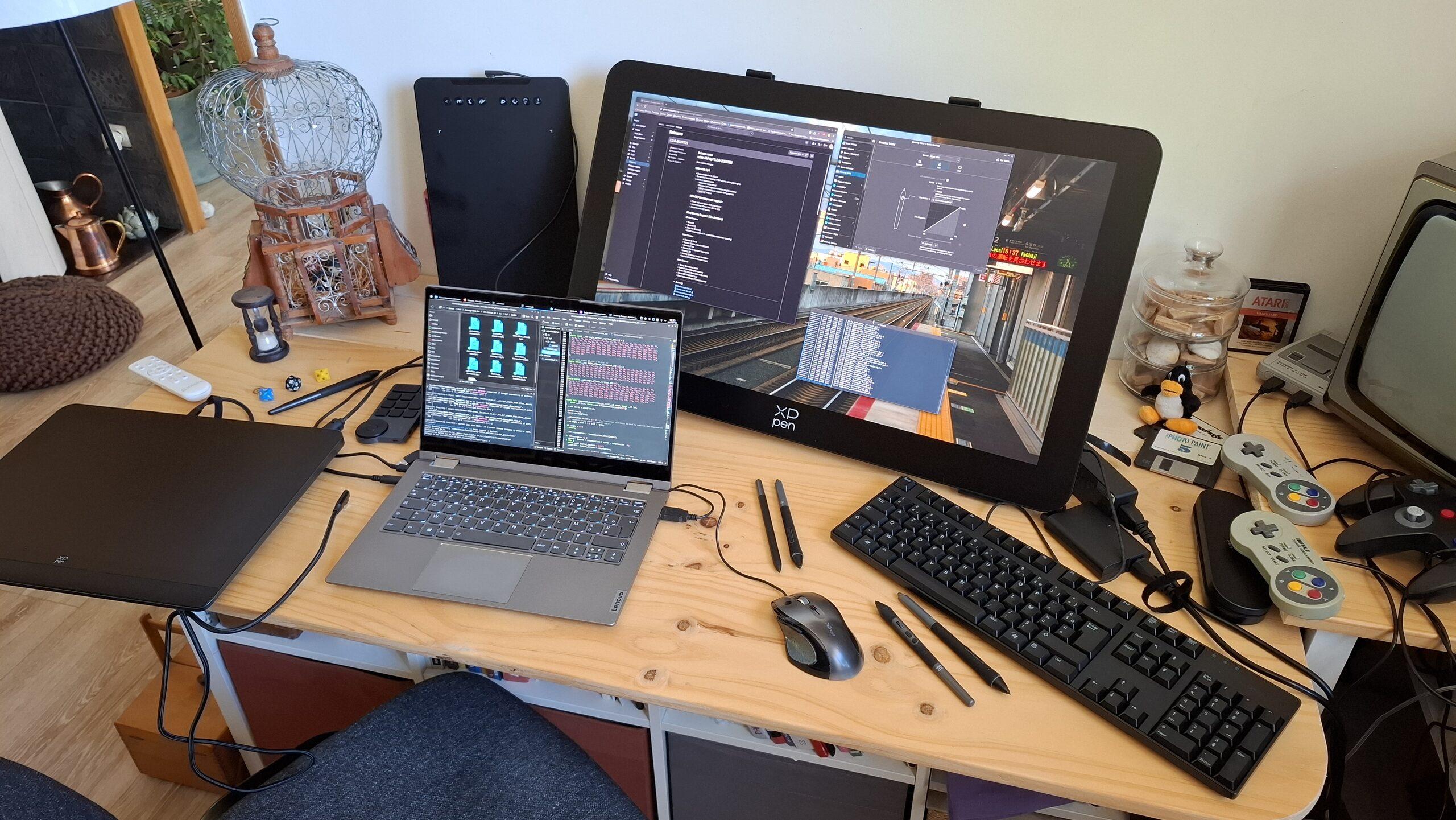 My "dev workbench setup" with laptop displaying code and directories (kate, a konsole for compiling and dolphin to see the file changed), surrounded by multiple drawing tablets (the Artist Pro 16 gen2, the Deco 01V3 , to test the bpf support too during dev). In the middle, a large 27-inch XpPen Artist Pro (gen2) tablet dominates the desk. Around some decoration for the shooting of the video review: RPG dices, an old TV, and controller of super nes and n64. A little plushie of tux also seat in a corner.