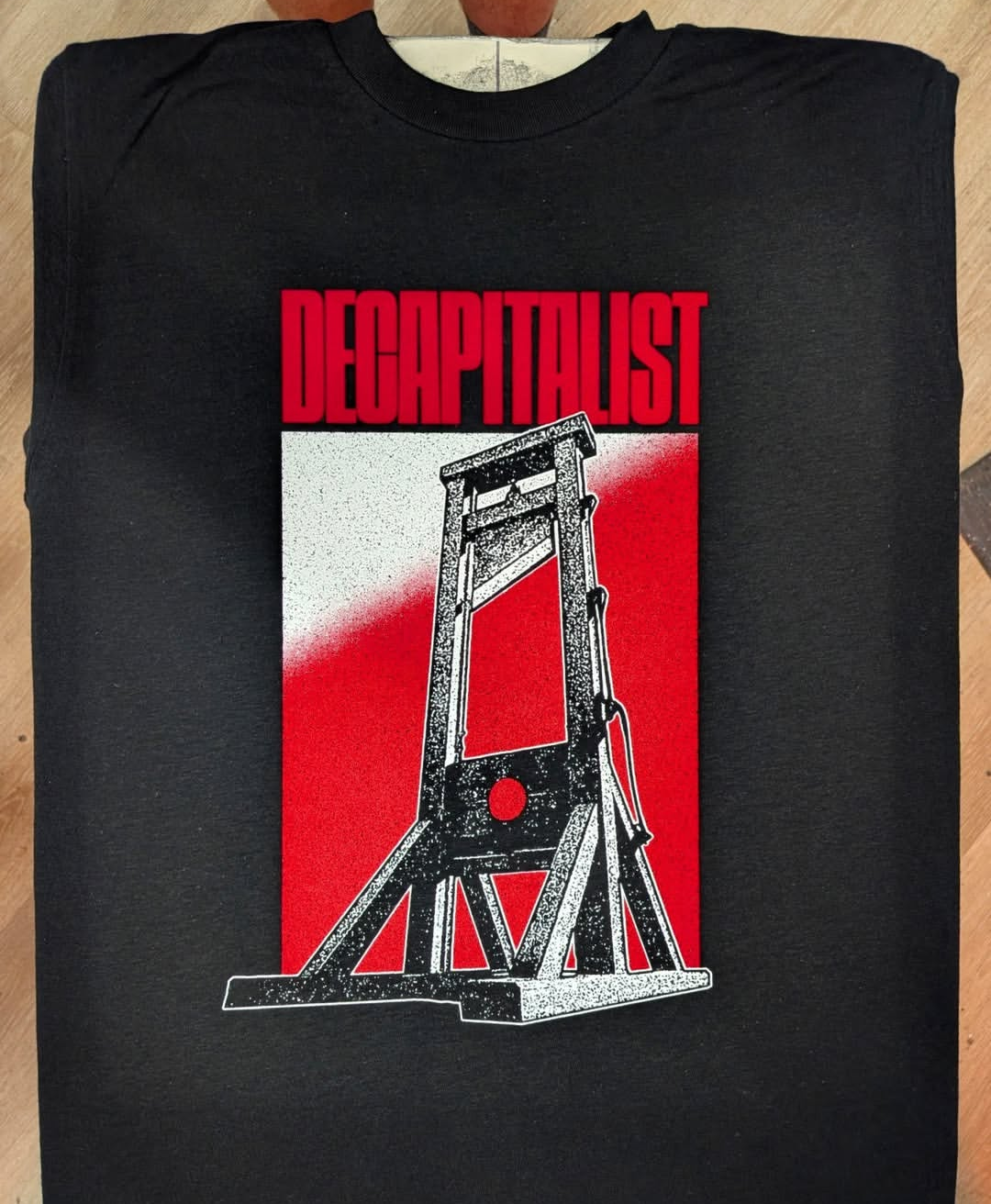 Maglietta nera con scritta rossa "DECAPITALIST" e immagine di una ghigliottina.
