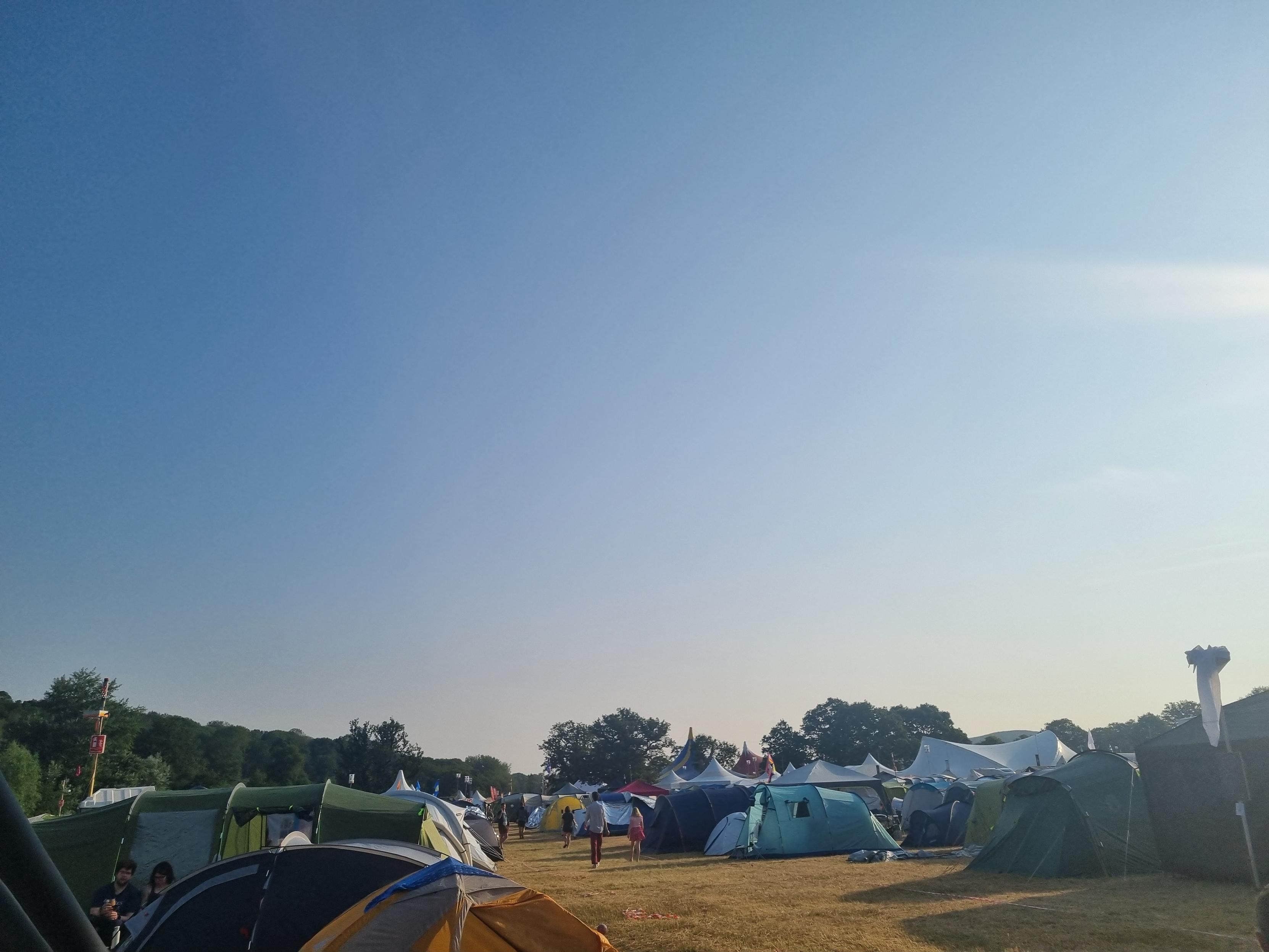 The morning sky over the same scene. Hundreds of brightly coloured tents. The sky is very blue with some high wispy clouds on the right