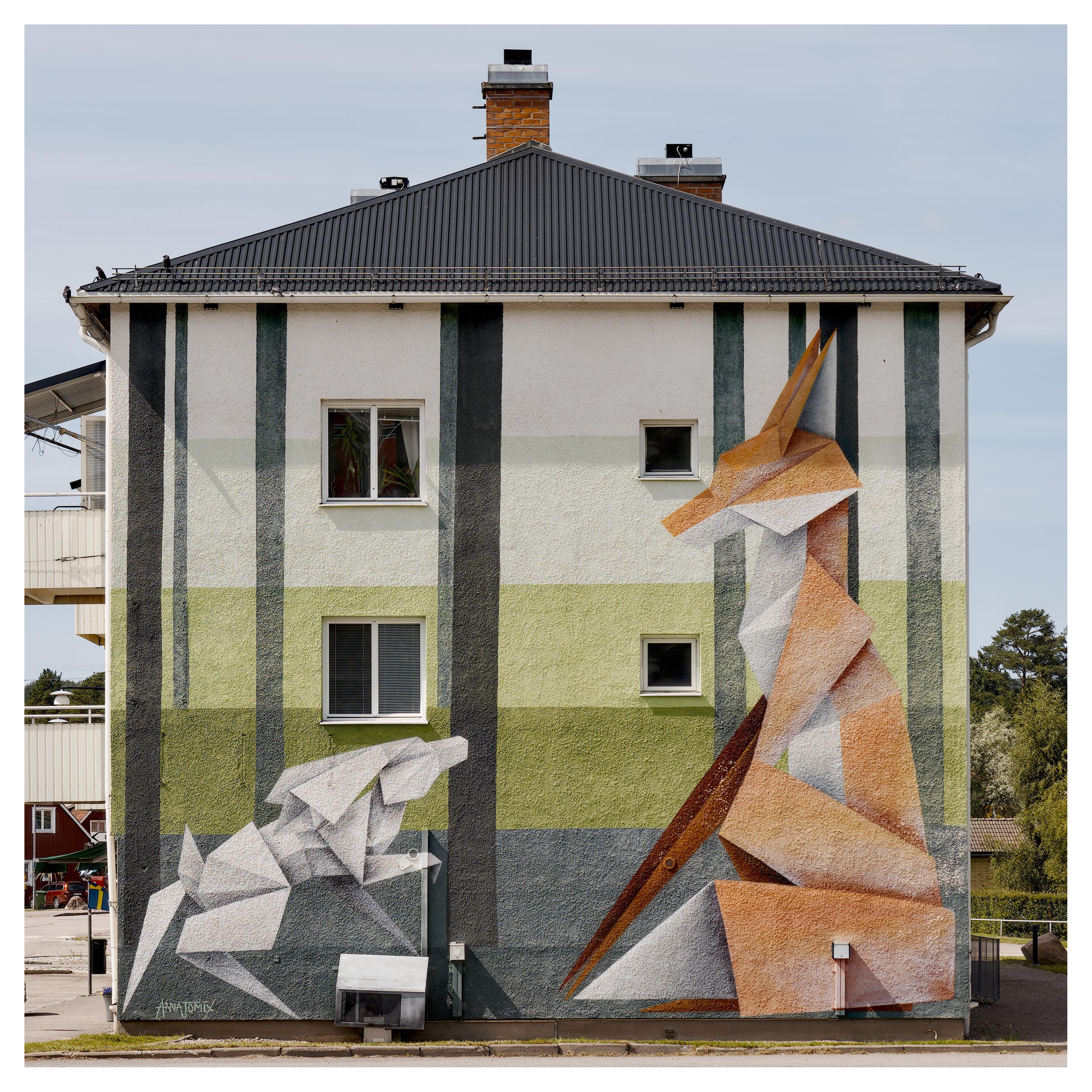 En stående bild på en husv6med en målning av en vit har och orange räv, båda som om de var origami. Väggen har två gröna horisontella linjer. Fyra fönster på två våningar.