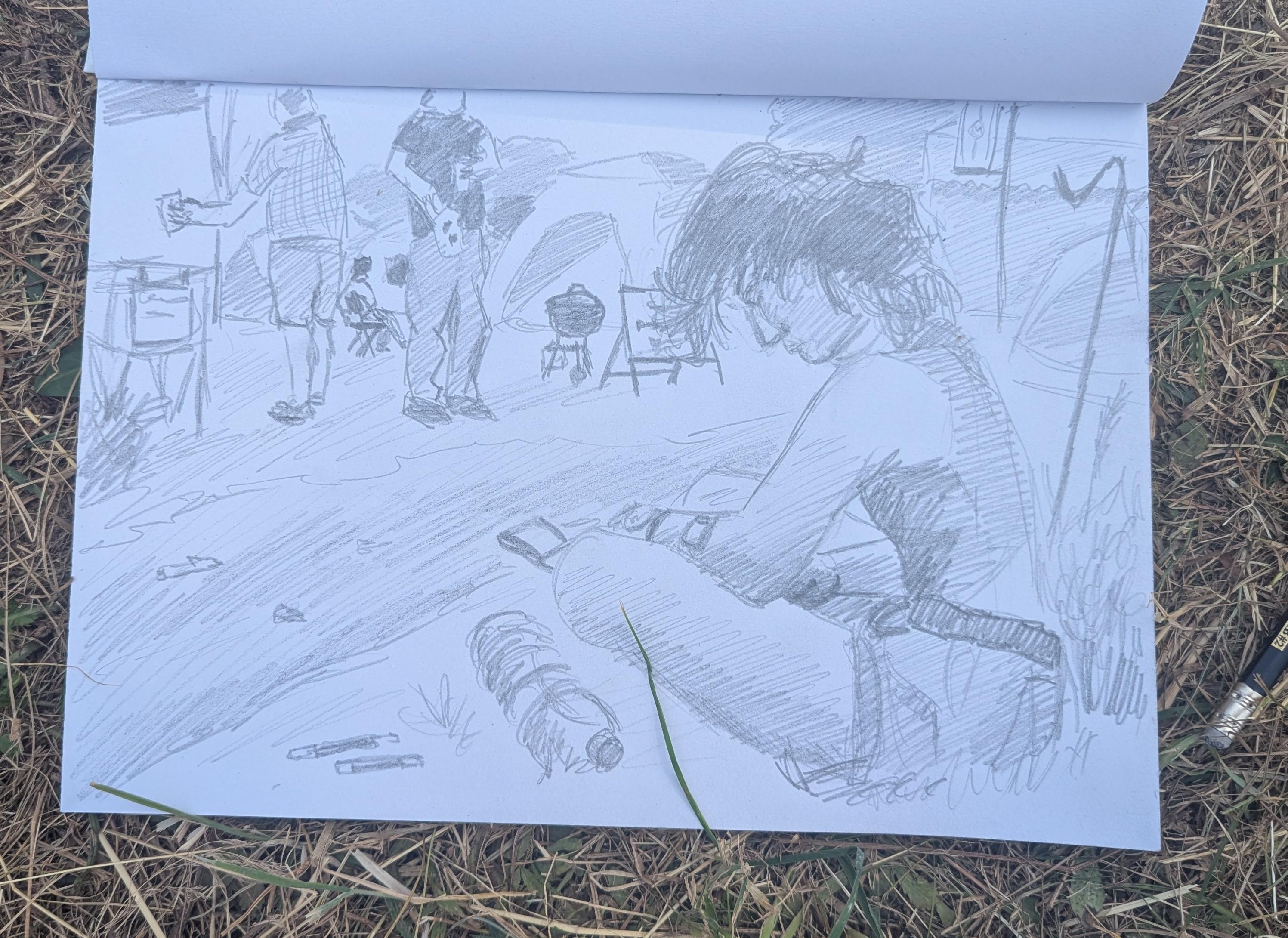 A pencil drawing of someone sat by a path doing urban sketching. In the background are some people, tents, tables and a barbecue