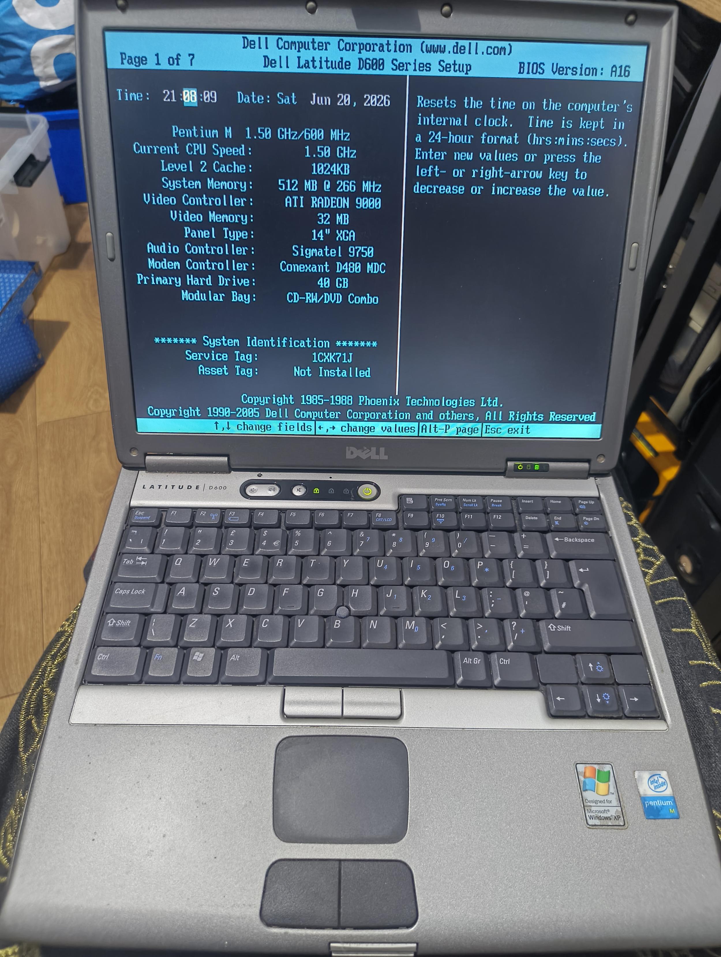 A Silver Dell Latitude  D600 Showing a Bios Screen, SIlver laptop, grey keyboard, blue & blacks screen showing system specs