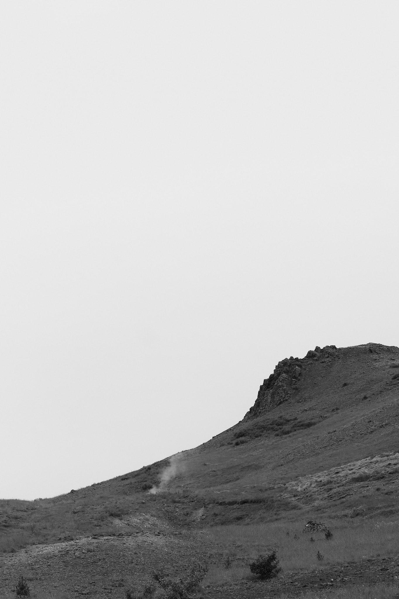 A black and white photo of the mountainside. Steam rises from a geothermal spring.