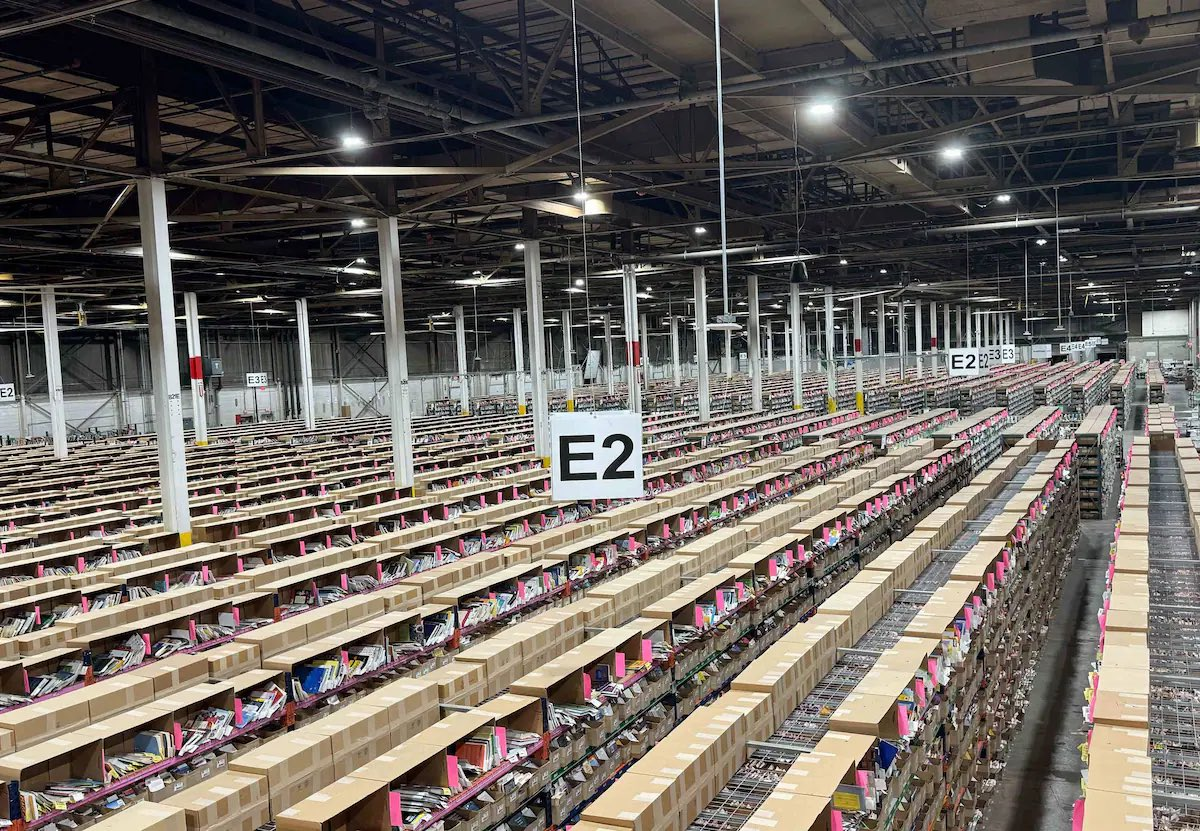 Photo of a huge warehouse with rows and rows of tables covered in thousands of boxes of books.