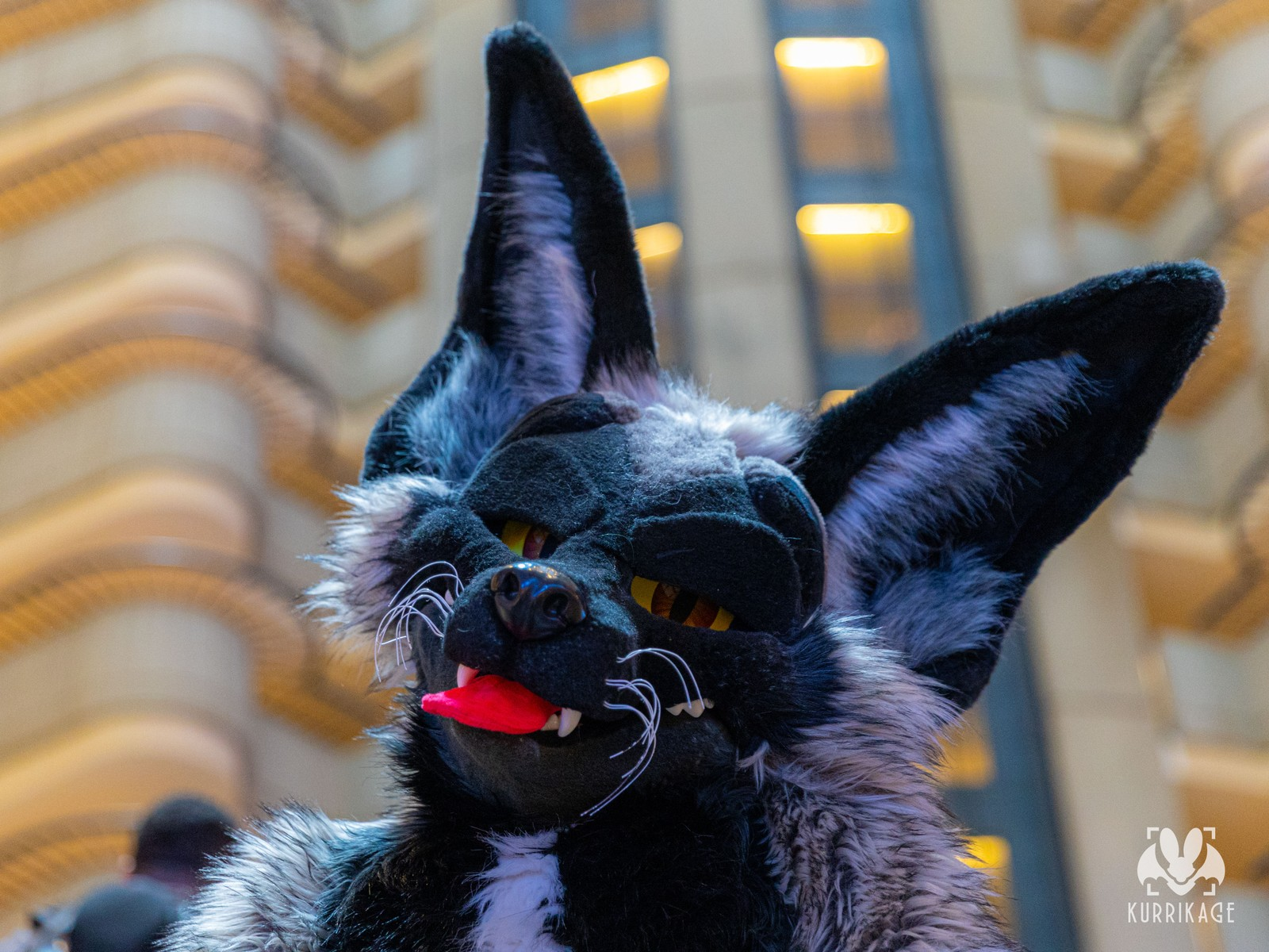 A headshot of a fox fursuiter with their tongue out against the iconic interior ribcage of the Atlanta Marriott Marquis.