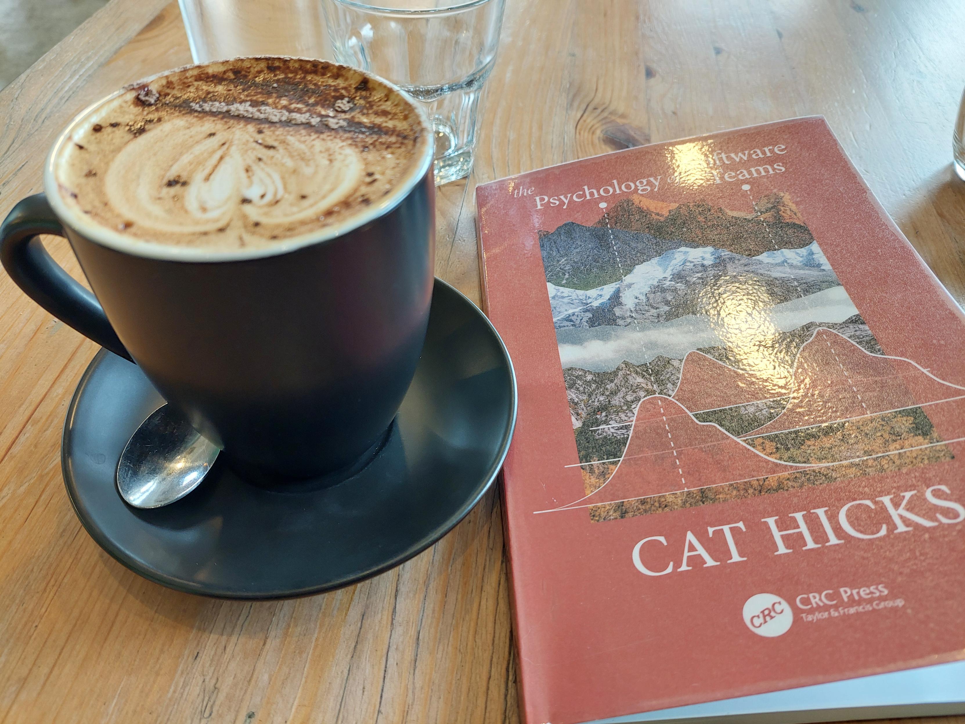 Mug of coffee on a table next to a book with the title, 'The Psychology of Software Teams' by Cat Hicks, CRC Press (Taylor & Francis Group).