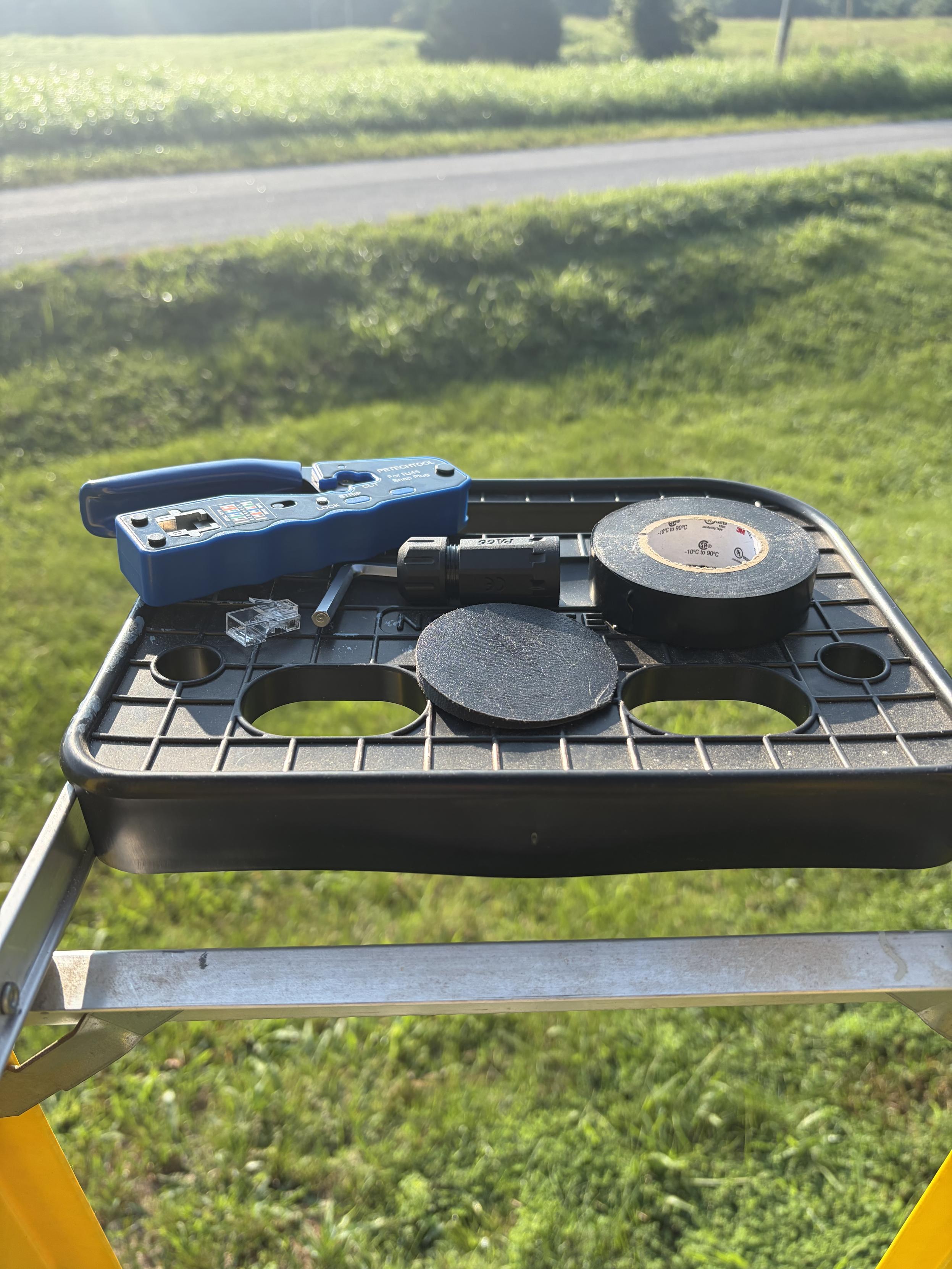 Crimper, tape, wedge, rj45 connector, and hex key layer out on top of a ladder