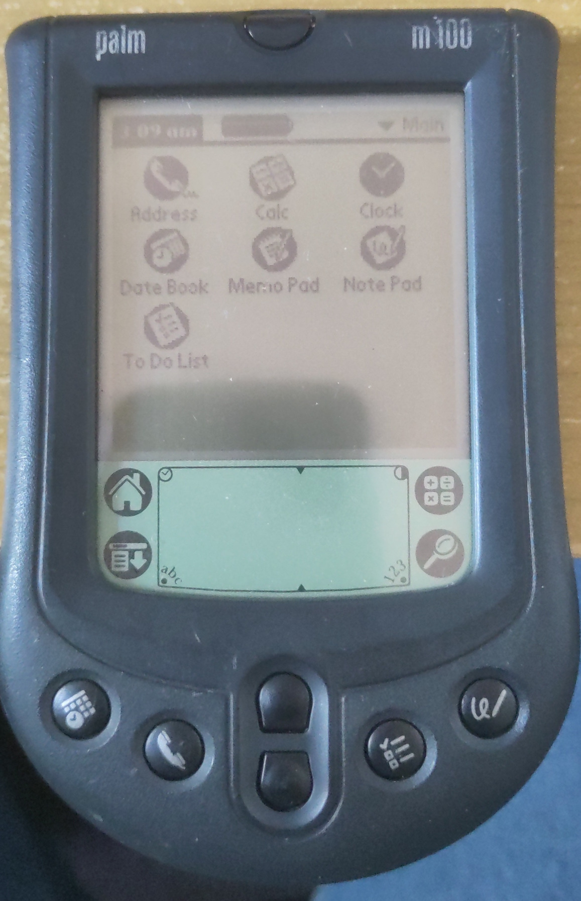A slightly battered Palm m100 PDA. It is switched on, and icons for various programs are visible on the screen.