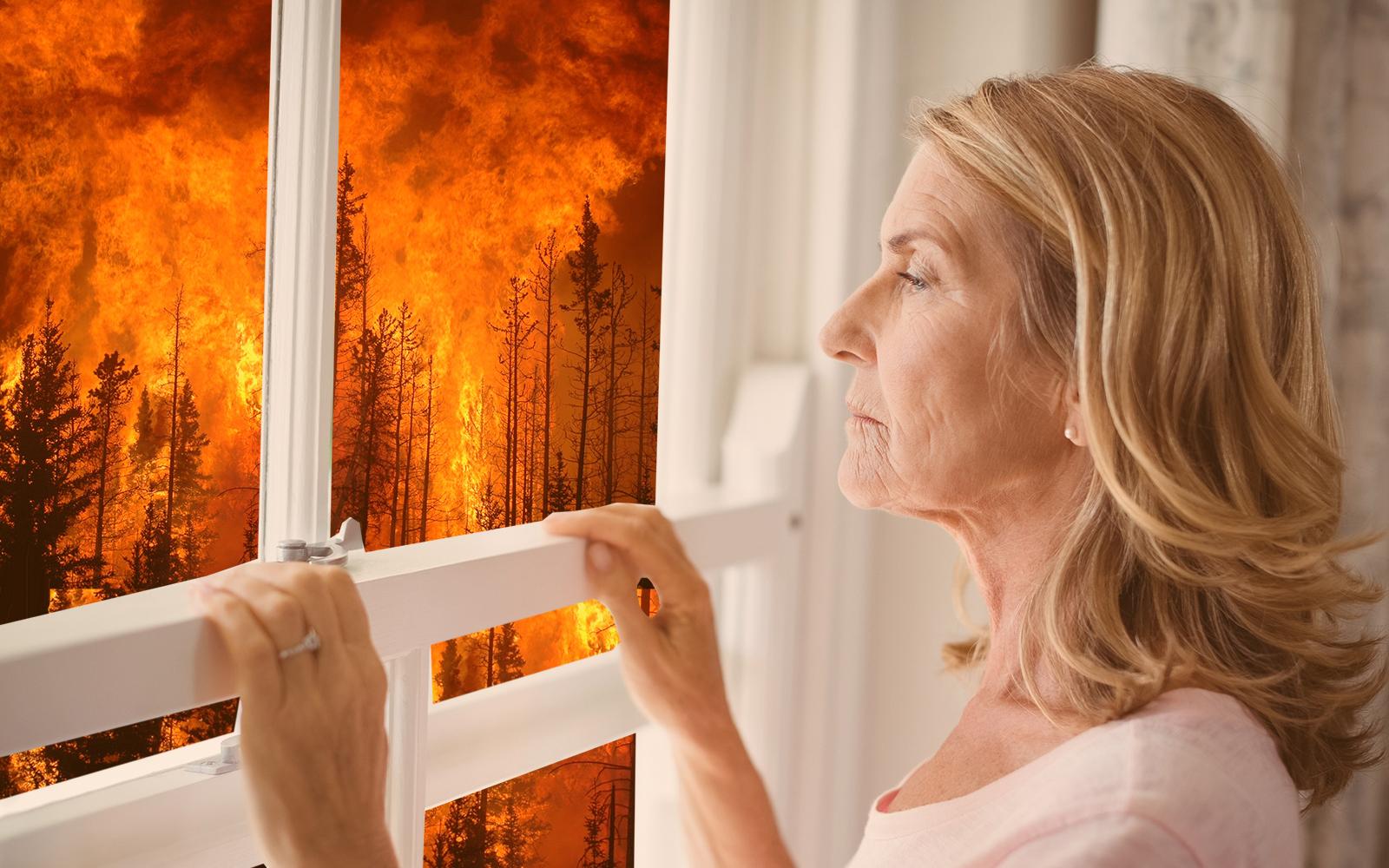 Older white blonde woman looking judgmentally out of living room window at flaming forest