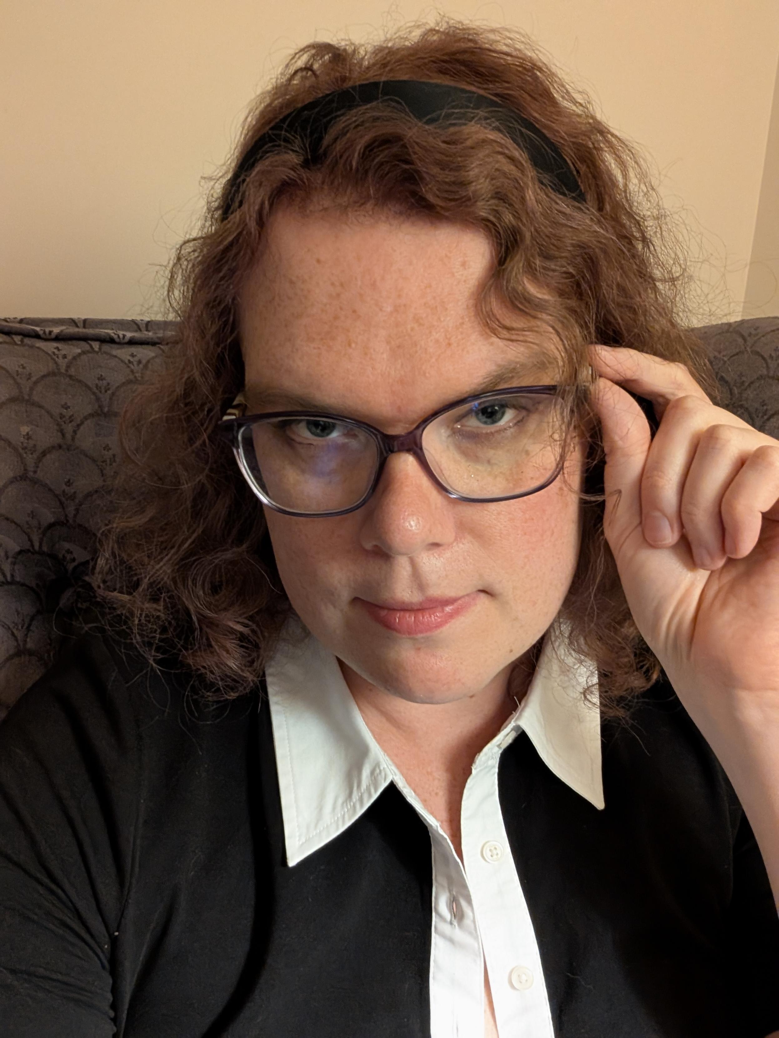 Christine holds onto her glasses and looks into the camera