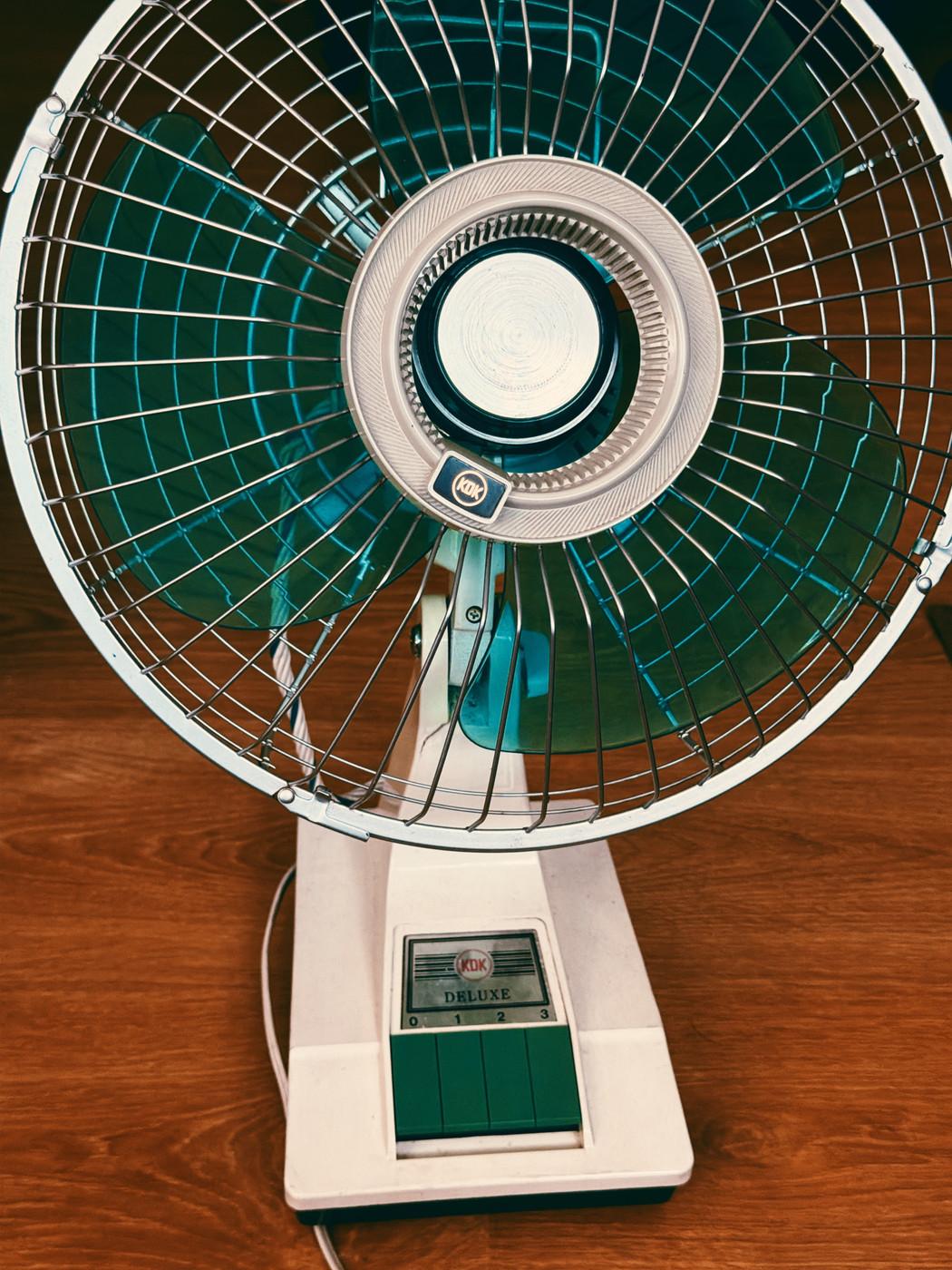 Vintage KDK Deluxe electric table fan with blue blades and a white base, placed on a wooden surface.