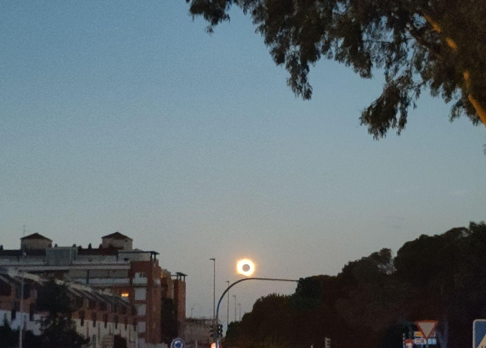 The sun, about to set, is completely blocked by the moon, with a bright corona around it still lighting up the surroundings brighter than the full moon.