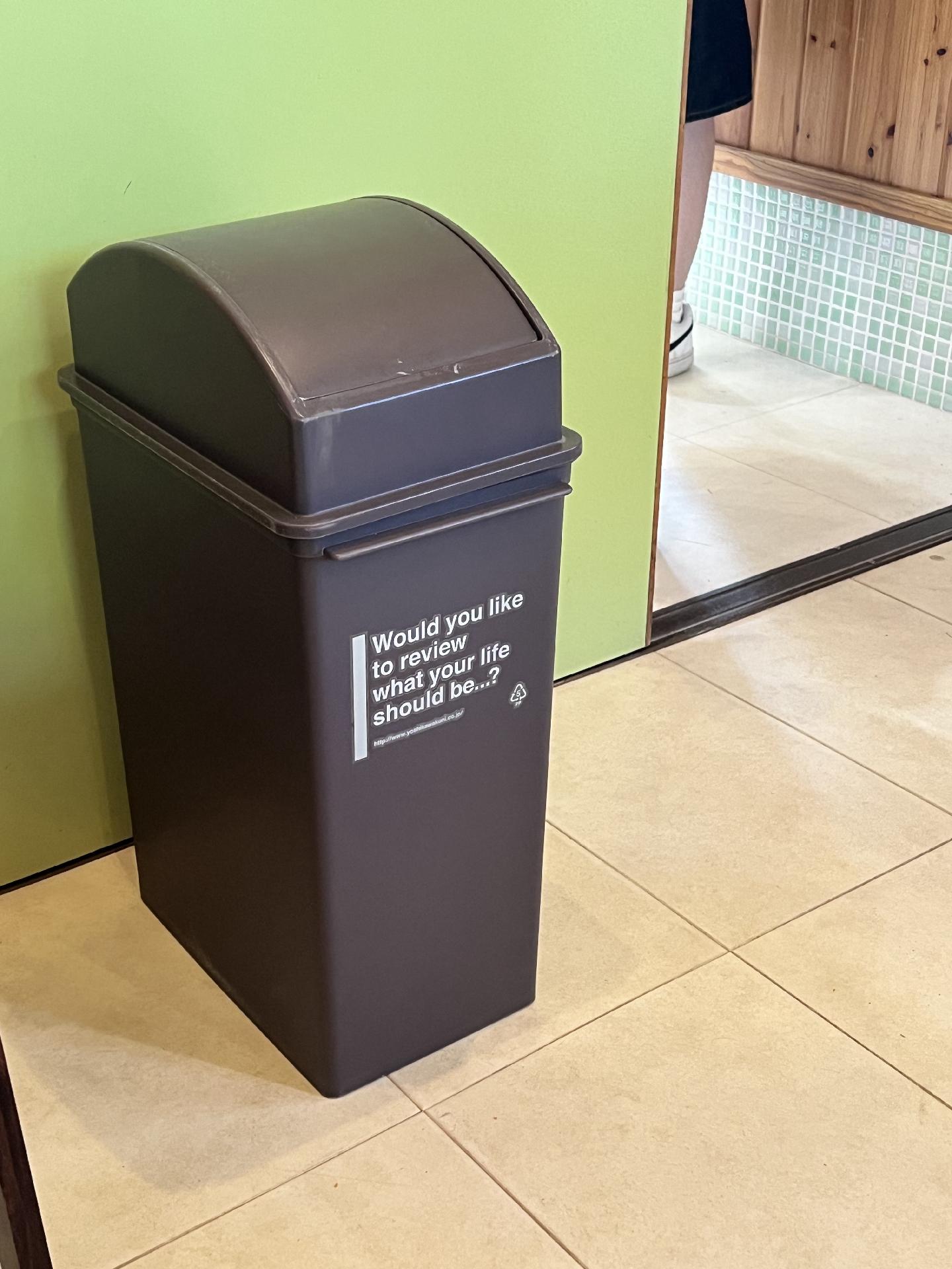 A black trash can with writing that reads “would you like to review what your life should be…?”