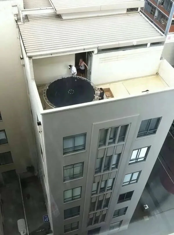 Three people setting up a trampoline on the small rooftop terrace of a tall building.