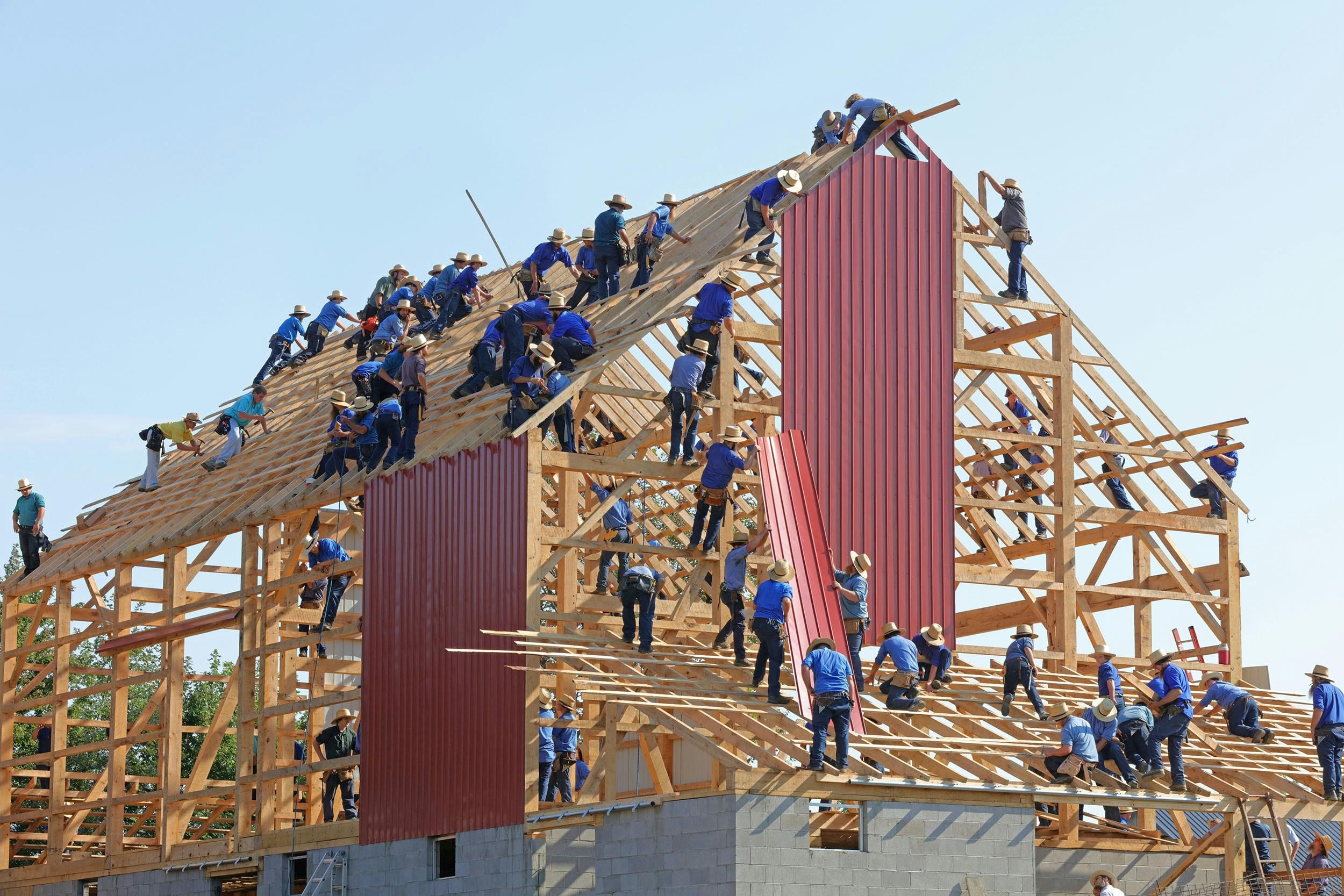 Photo is by photographer Randy Faith via Unsplash. It depicts dozens of people building a barn together.