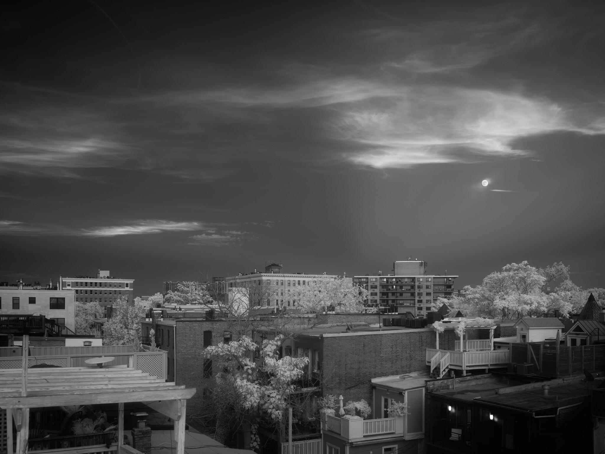 Clouds and a moon against a dark sky, over urban rooftops