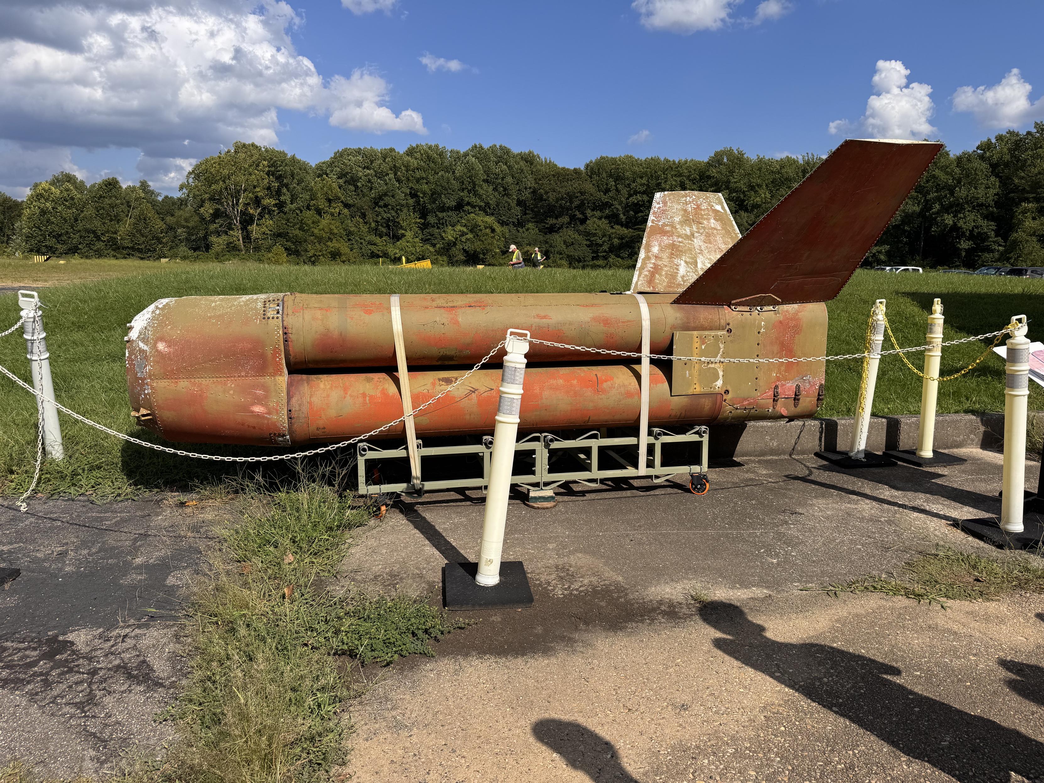 An old shell of a Nike Hercules missile primary stage, covered in rust and missing two of its 4 fins. It sits on its side, roped off but on display.