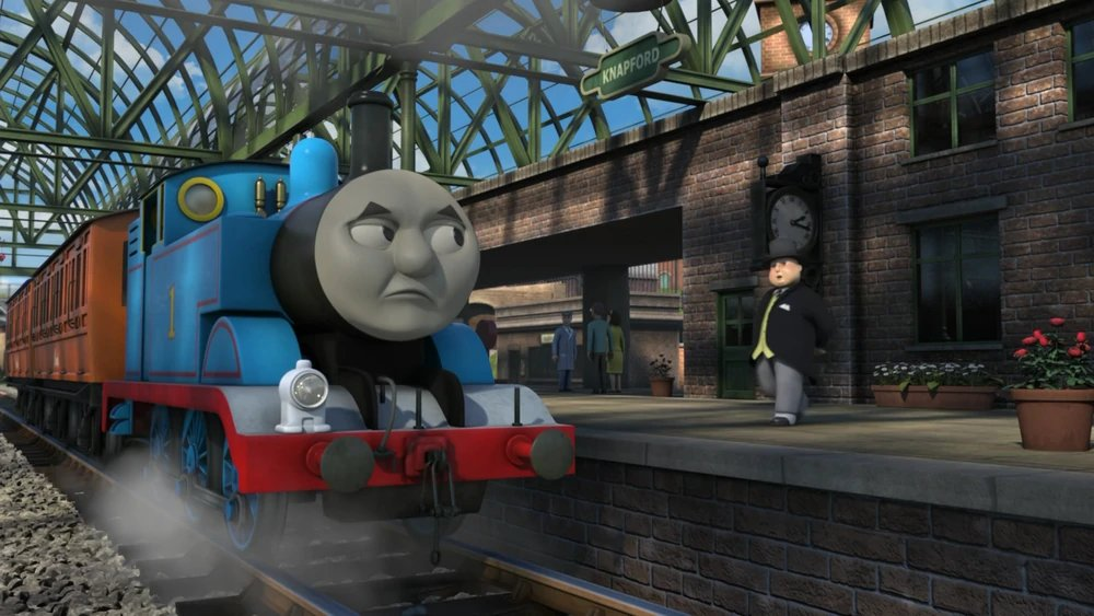 Thomas the tank engine at a station platform looking miffed at the charactor known as “the fat controller”.