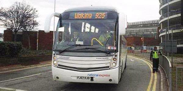 The front of a white National Express coach on a road. The electronic destination and route is set as “Woking 925”