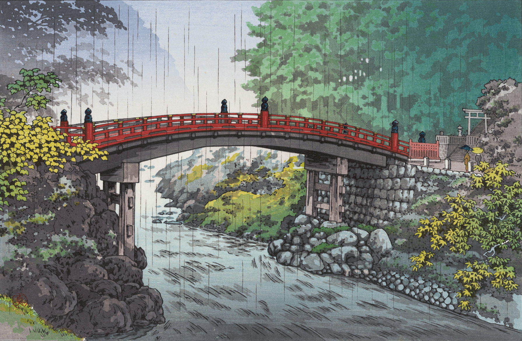A view looking toward Nikko's Shinkyo Bridge on a rainy day. The red-lacquered bridge spans the Daiya River in a short, curving arc; healthy-looking green trees and shrubs crowd in close to the stone foundations on either side. Beyond the bridge, the steep tree-covered mountain landscape fades away into the mist; above, the sky is overcast, and rain continues to fall on the scene.