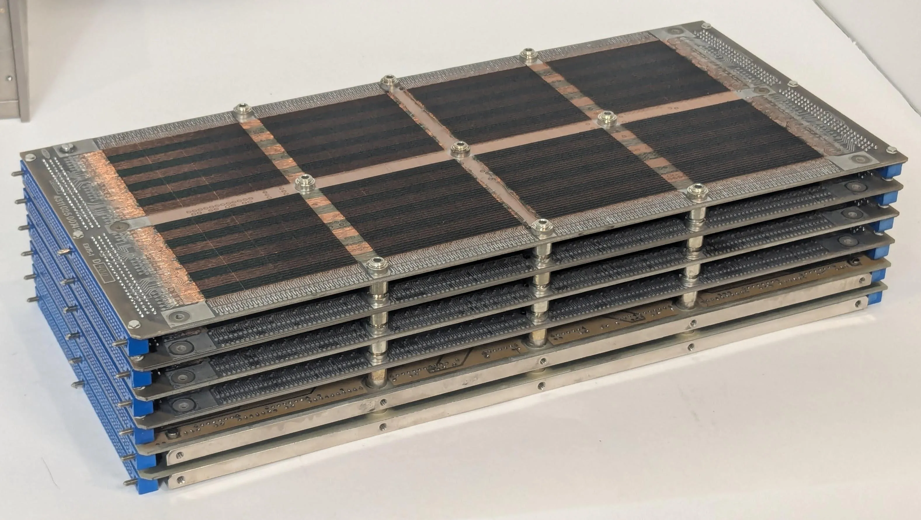 The core stack from the Spacelab computer. This is a stack of six rectangular circuit boards, joined by blue connectors on each end. The cores are visible on the top board. The 294,912 cores are way too small to see; there are eight large reddish-brown squares, each holding a region of cores. 18 reddish and greenish stripes are slightly visible, showing regions for the 18 bits of storage.