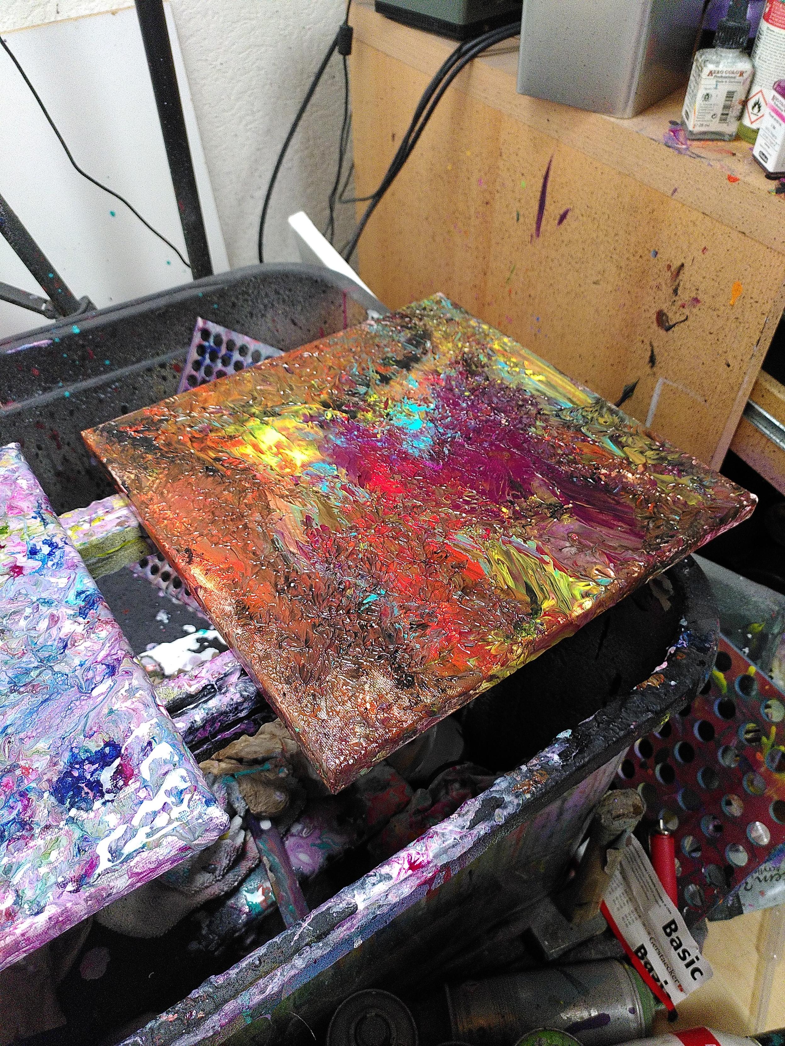 an abstract painting next to other one with a strong contrast of an abstract purple red figure in what looks like trapped in flames. Towards the edges, the painting has more dark areas, with orange and yellow flames shining still active