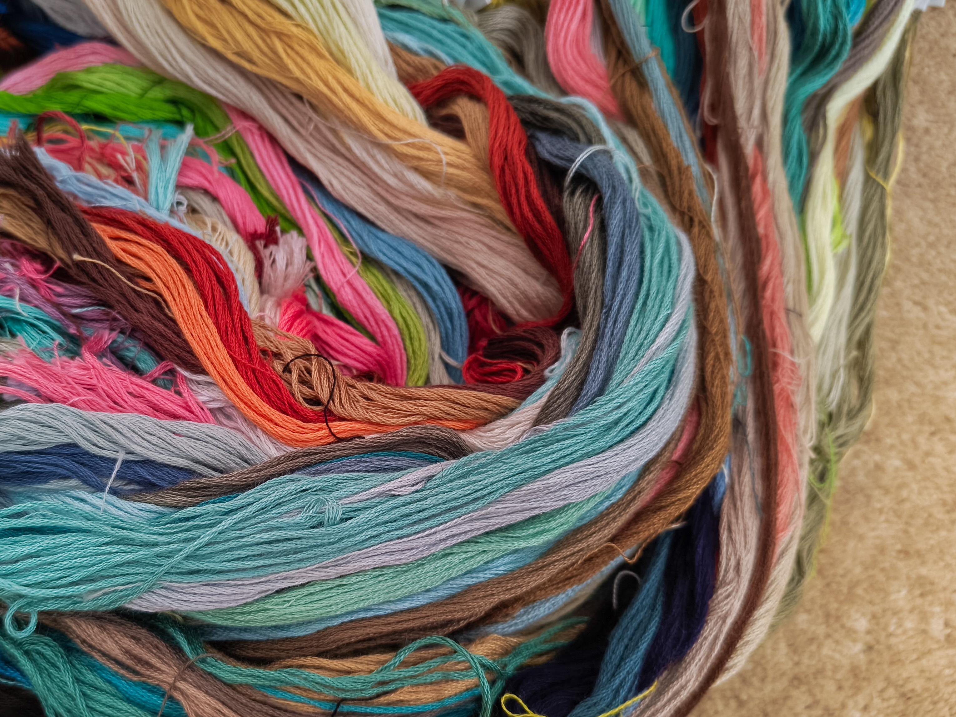 Close up on a pile of long embroidery threads skeins in various colours, all twirled together in a deeply disorganised fashion