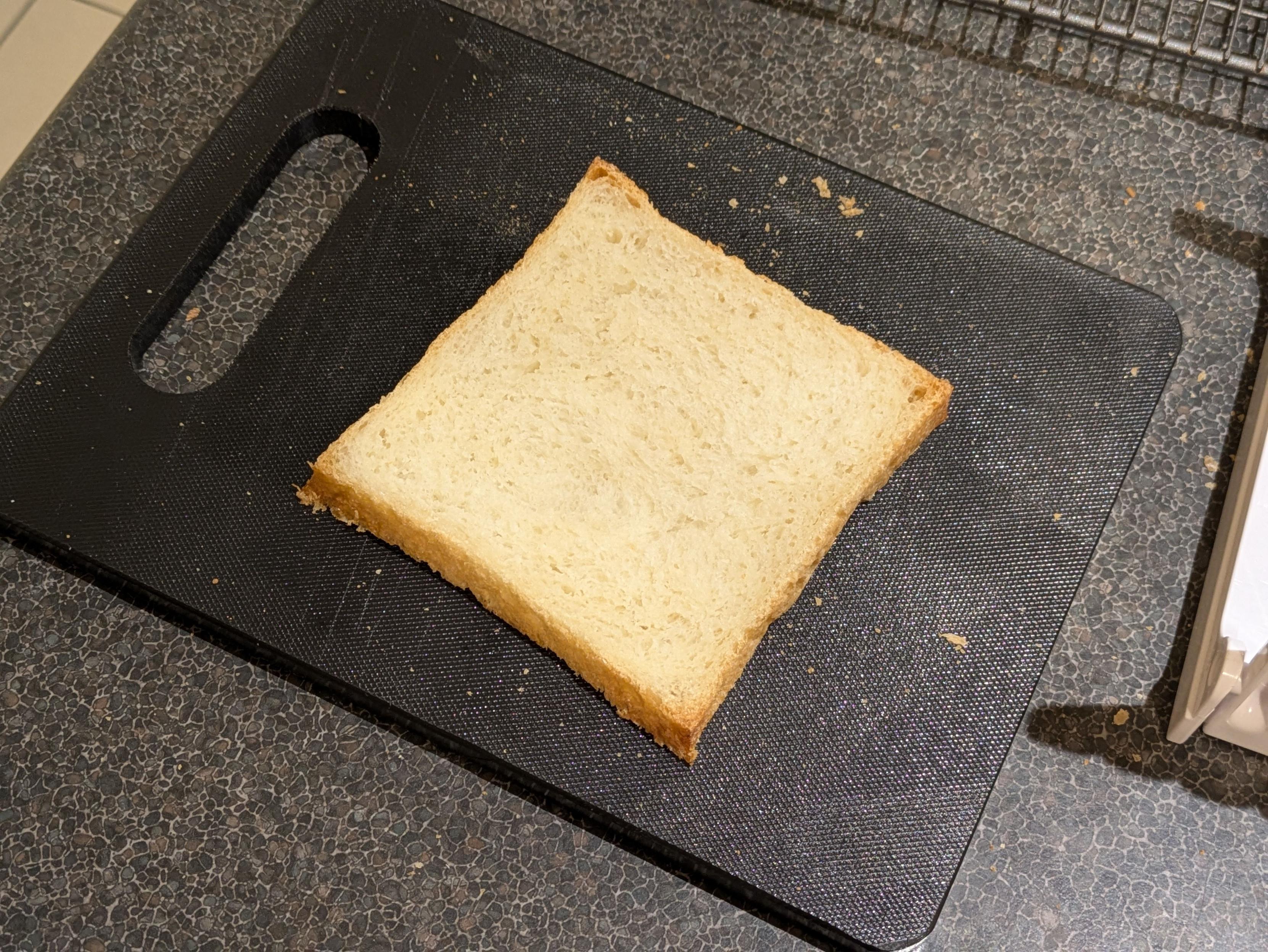 A photo of an unsettlingly perfectly square slice of bread on a cutting board. There's no curvy edges or obvious top side to it.