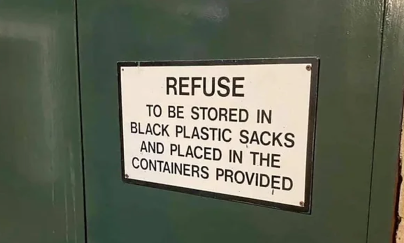 Photo of sign against a dark green wall which reads: REFUSE  TO BE STORED IN  BLACK PLASTIC SACKS  AND PLACED IN THE  CONTAINERS PROVIDED