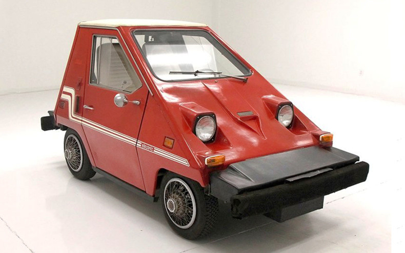 A very tiny triangle shaped red car with round headlights and a protruding black bumper.