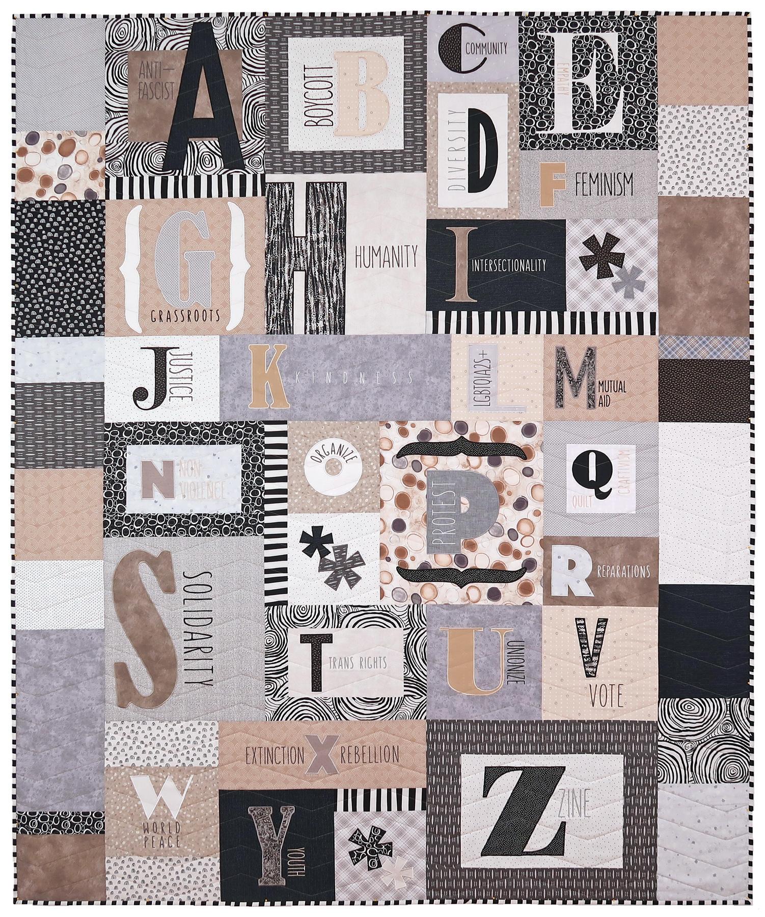 An abecedary quilt in neutral fabrics, like ecru, grey, black and white, shown in full. Each letter block (they are all different sizes and fonts) has a word associated with activism embroidered on it. List follows: A for anti-fascist, B for boycott, C for community, D for diversity, E for empathy, F for feminism, G for grassroots, H for humanity, I for intersectionality, J for justice, K for kindness, L for LGBTQIA+, M for mutual aid, N for non-violence, O for organize, P for protest, Q for quilt craftivism, R for reparations, S for solidarity, T for trans rights, U for unionize, V for vote, W for world peace, X for Extinction Rebellion, Y for youth and Z for zine.