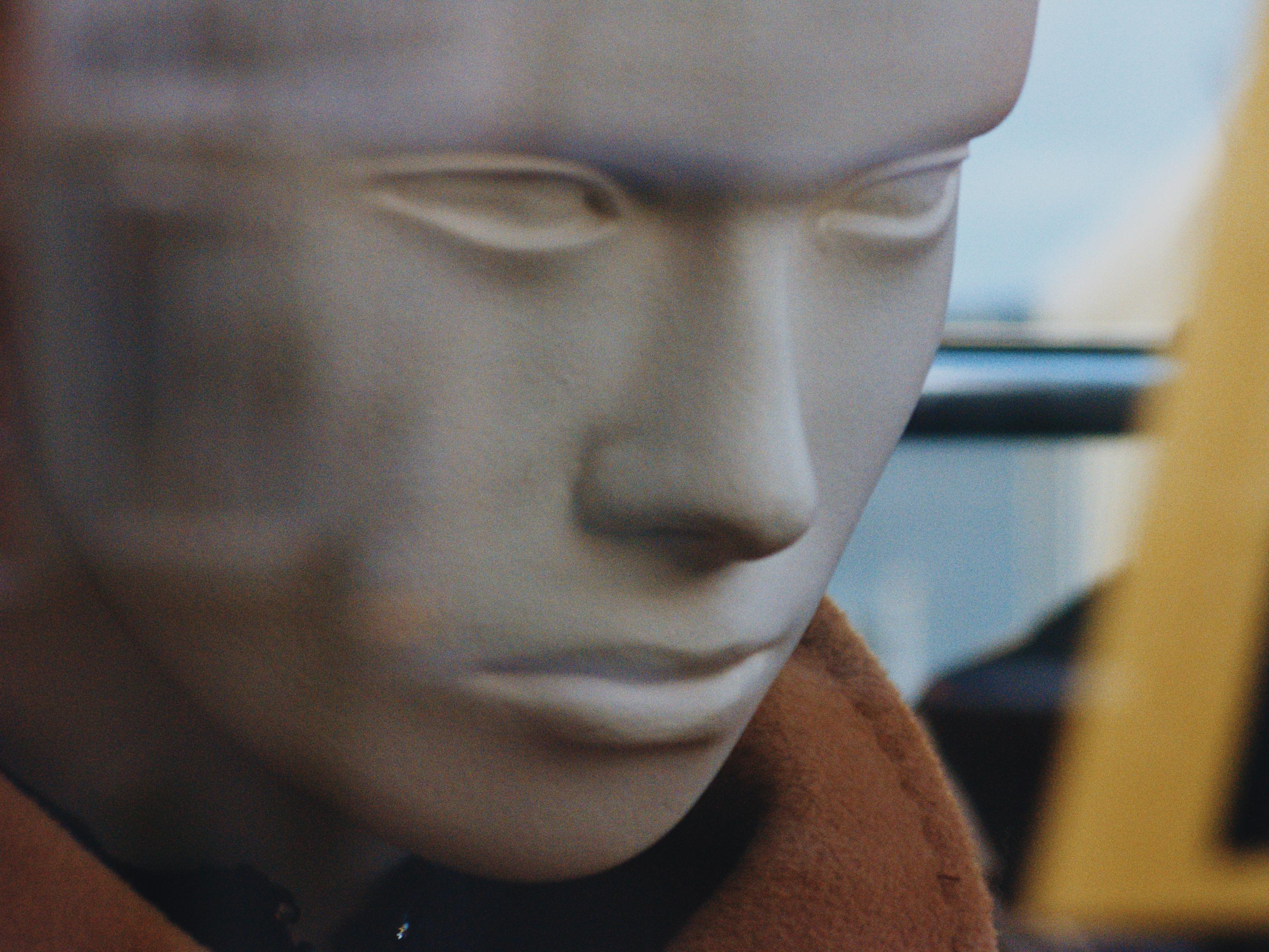A mannequin with a very serious look on its face seen through a shop window.